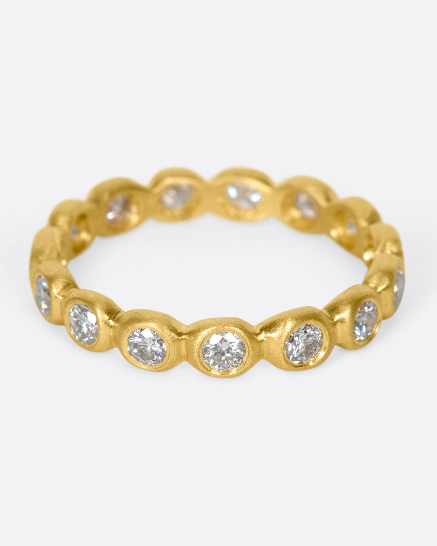 An eternity band of bezel set white diamonds in matte gold settings.