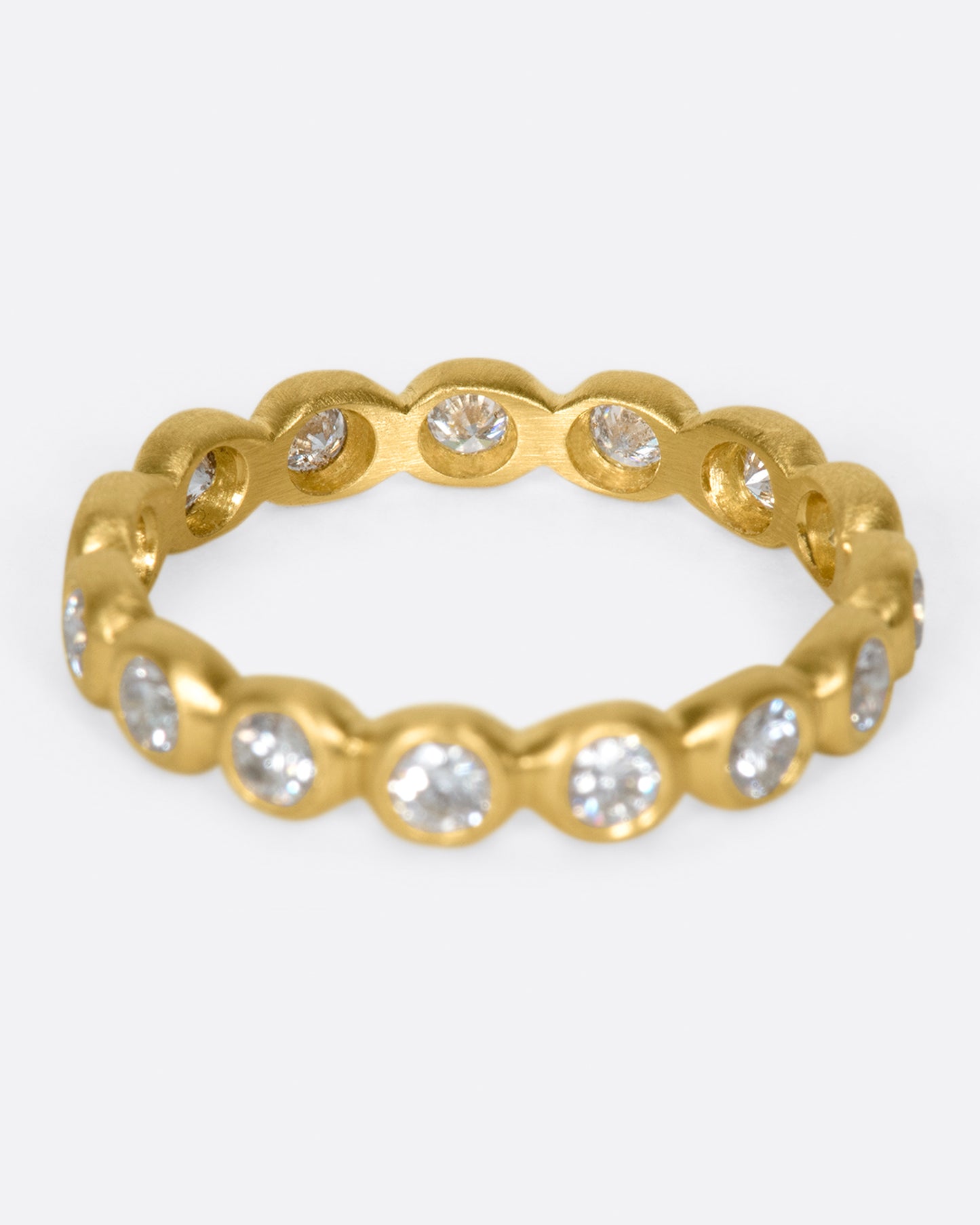An eternity band of bezel set white diamonds in matte gold settings.