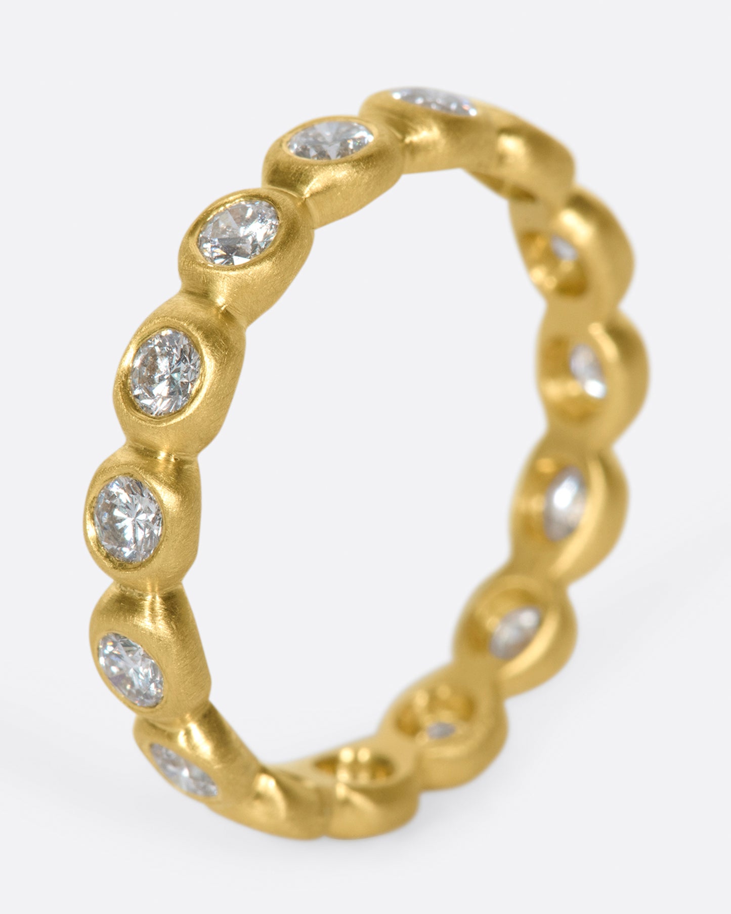 An eternity band of bezel set white diamonds in matte gold settings.