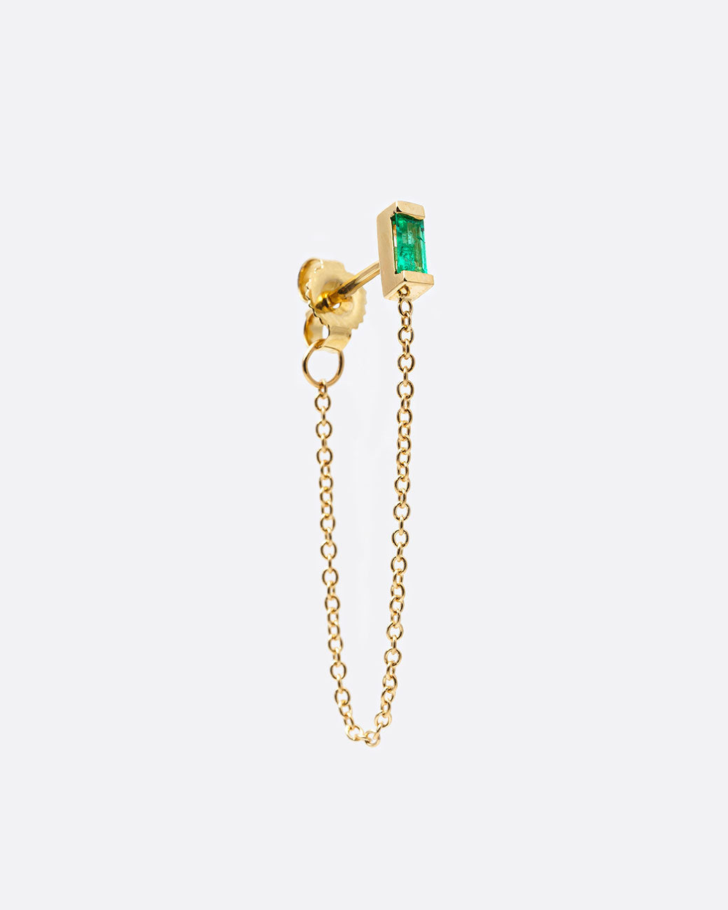 A yellow gold stud earring with a baguette emerald and cable chain that drapes from the bottom of the stud to the butterfly backing. Shown at an angle from the side.