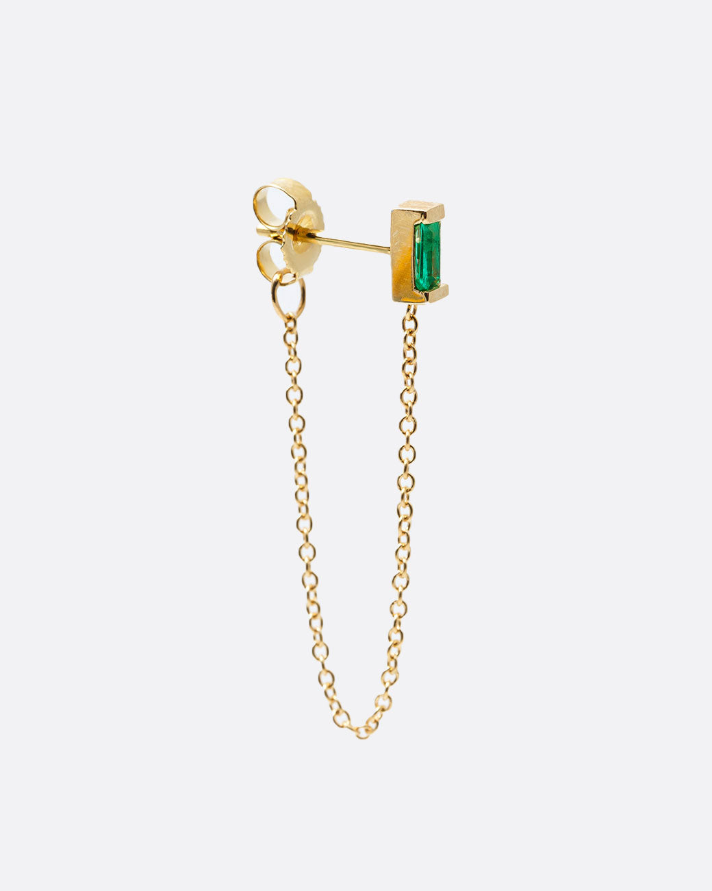 A yellow gold stud earring with a baguette emerald and cable chain that drapes from the bottom of the stud to the butterfly backing. Shown from the side.