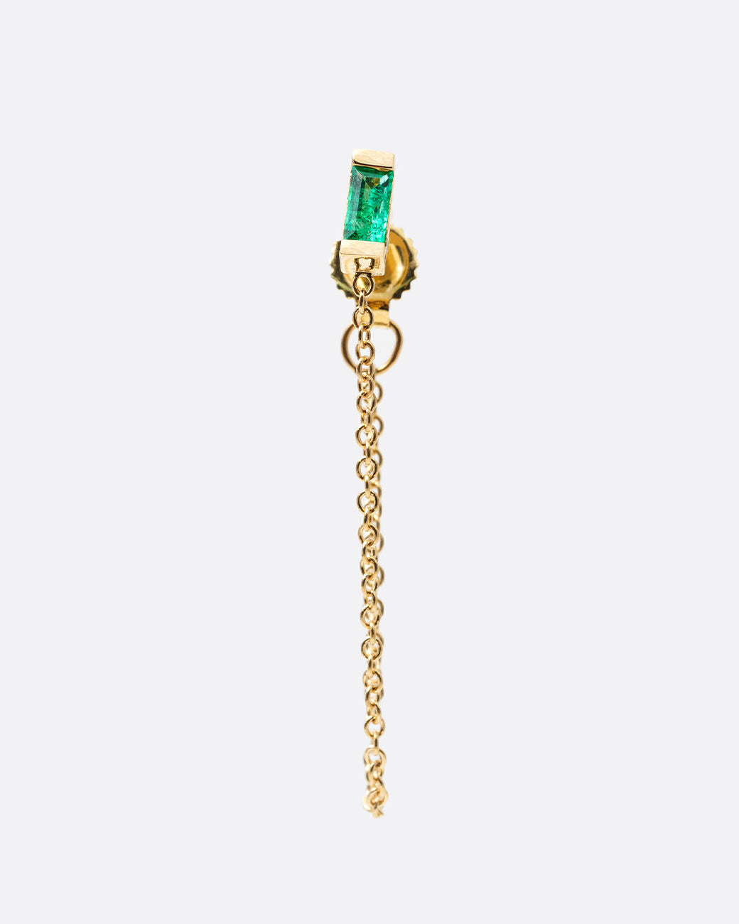 A yellow gold stud earring with a baguette emerald and cable chain that drapes from the bottom of the stud to the butterfly backing. Shown from the front.