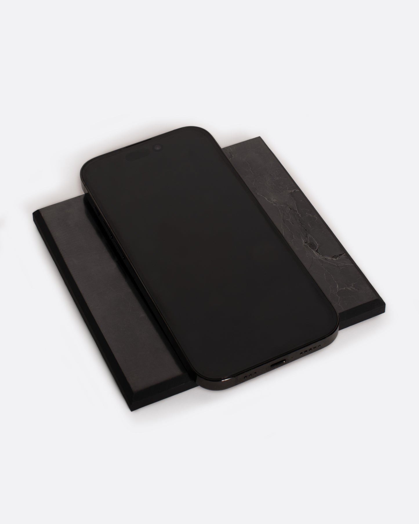A black stone tile with a cell phone lying on top. Shown lying flat at an angle from the top.