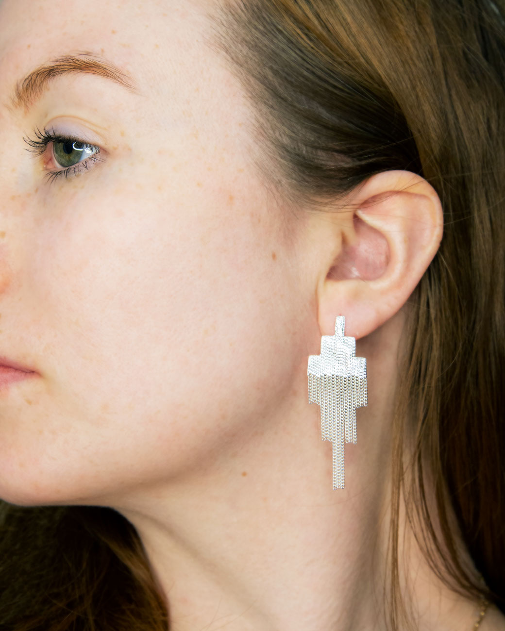 womans ear wearing the pixel earring. she is faced sideways, and looking into the distance. the pixel earring hangs about 1.5 inches below the earlobe.