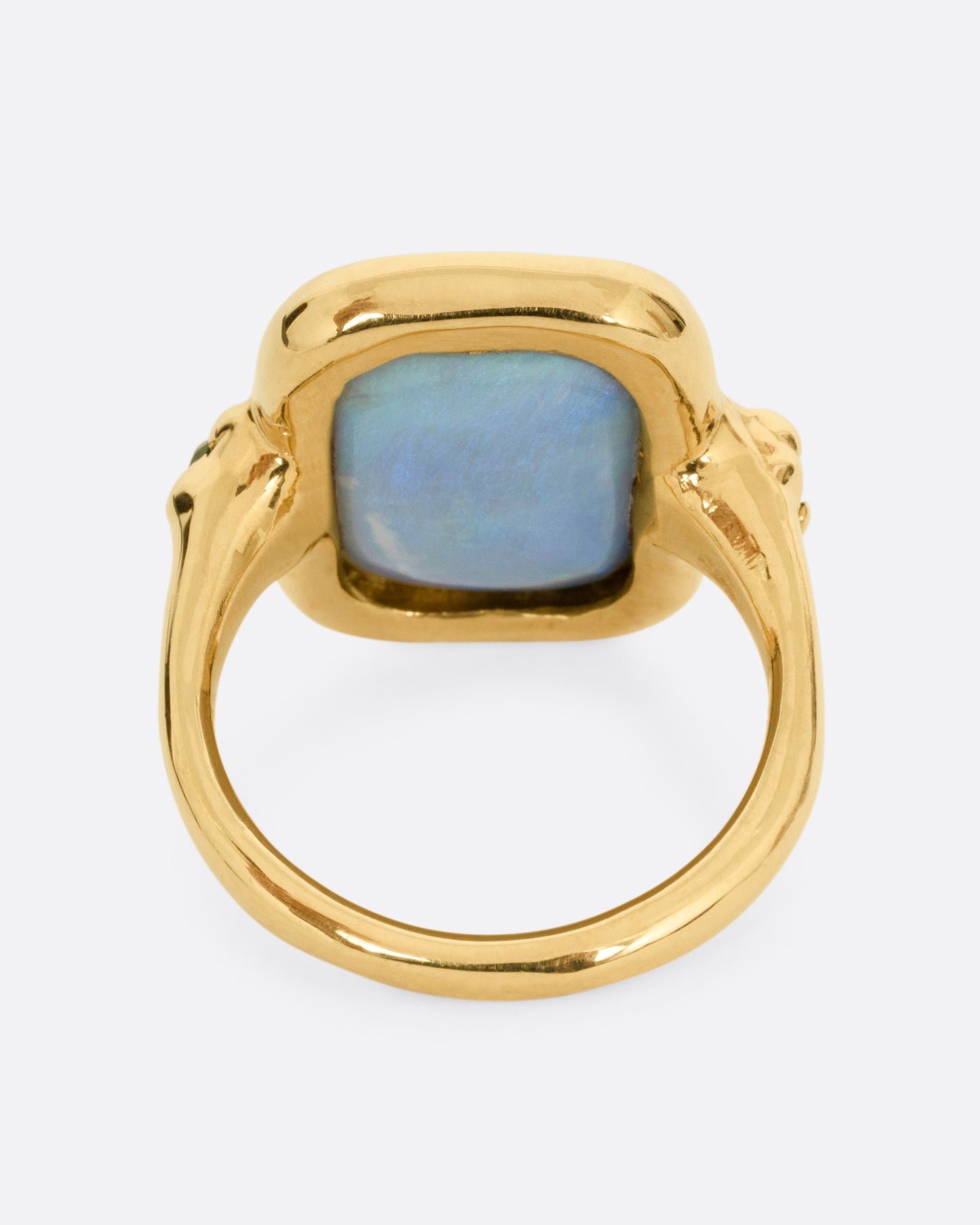 A yellow gold ring with a large rectangular boulder opal and emerald accents, shown from the back.