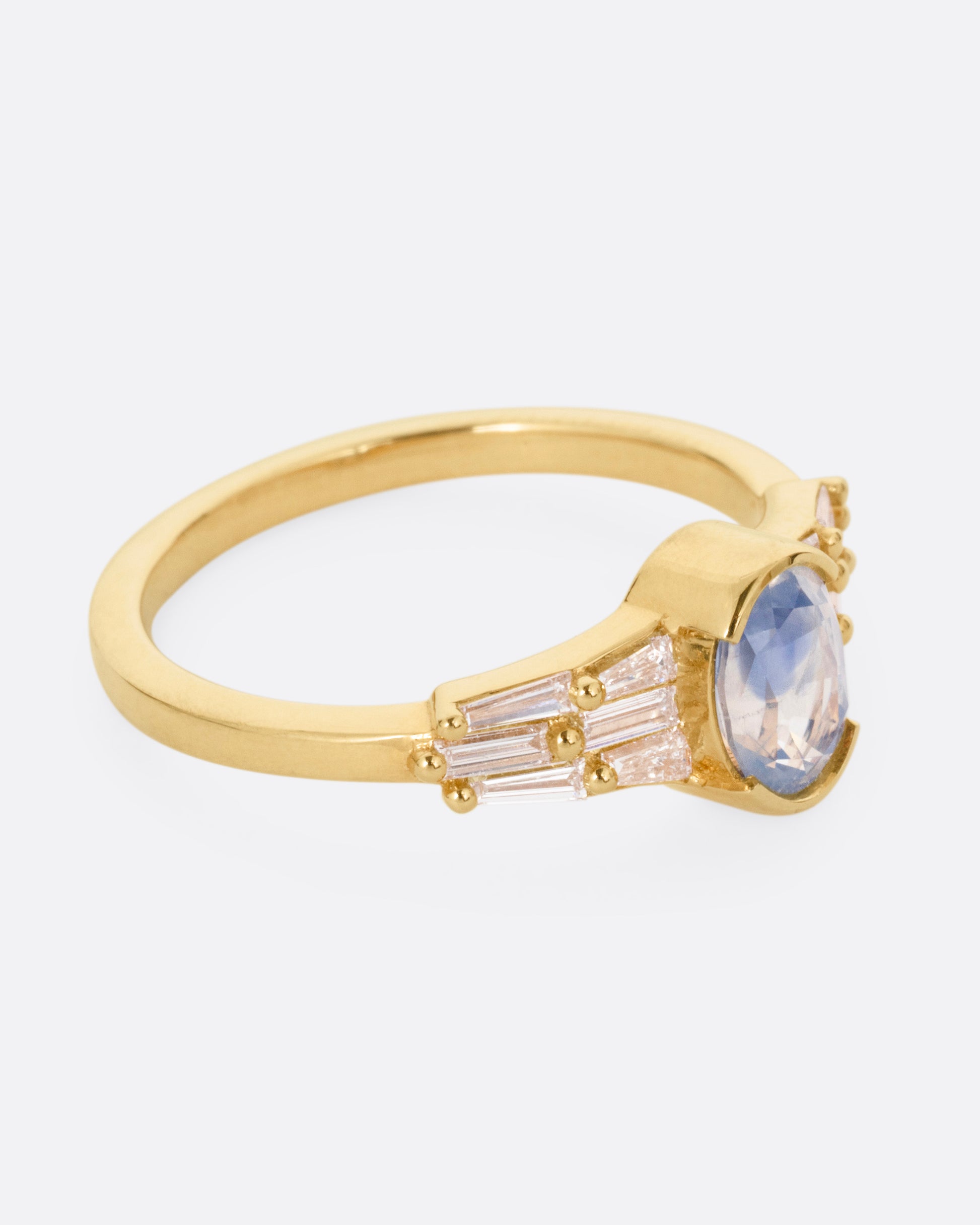 A yellow gold ring with stacked baguette diamonds and a bezel set sapphire, shown from the side.