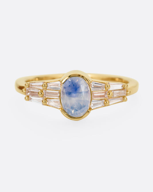 A yellow gold ring with stacked baguette diamonds and a bezel set sapphire, shown from the front.