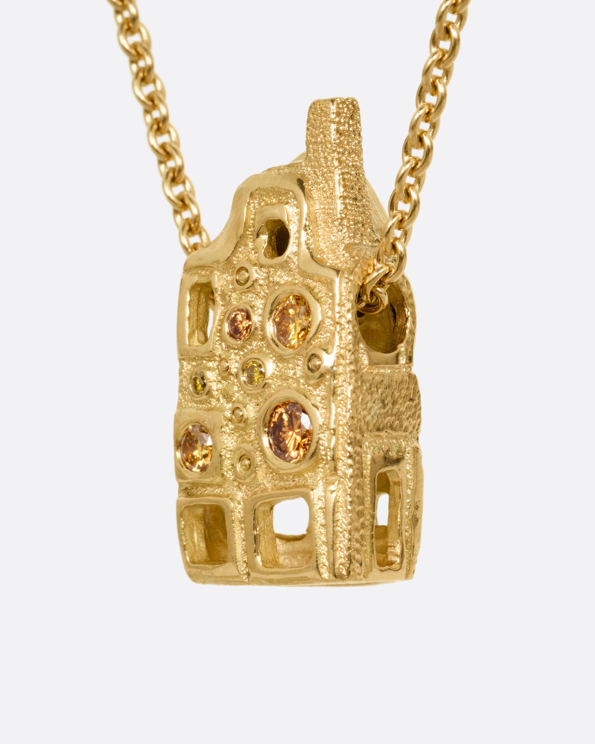 A yellow gold house-shaped pendant with multi-colored diamonds, on a cable chain, shown from the side. 