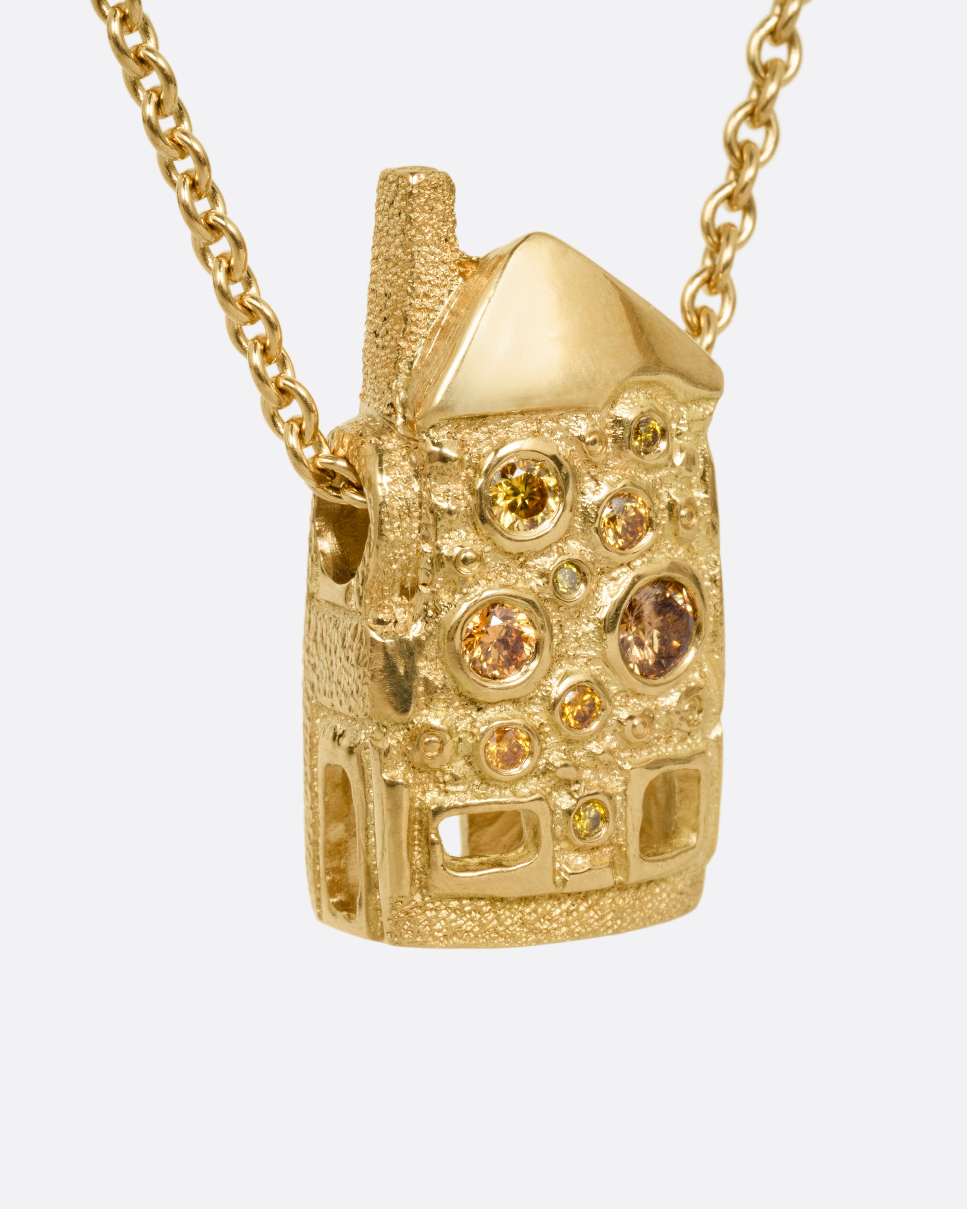 A yellow gold house-shaped pendant with multi-colored diamonds, on a cable chain, shown from the side. 