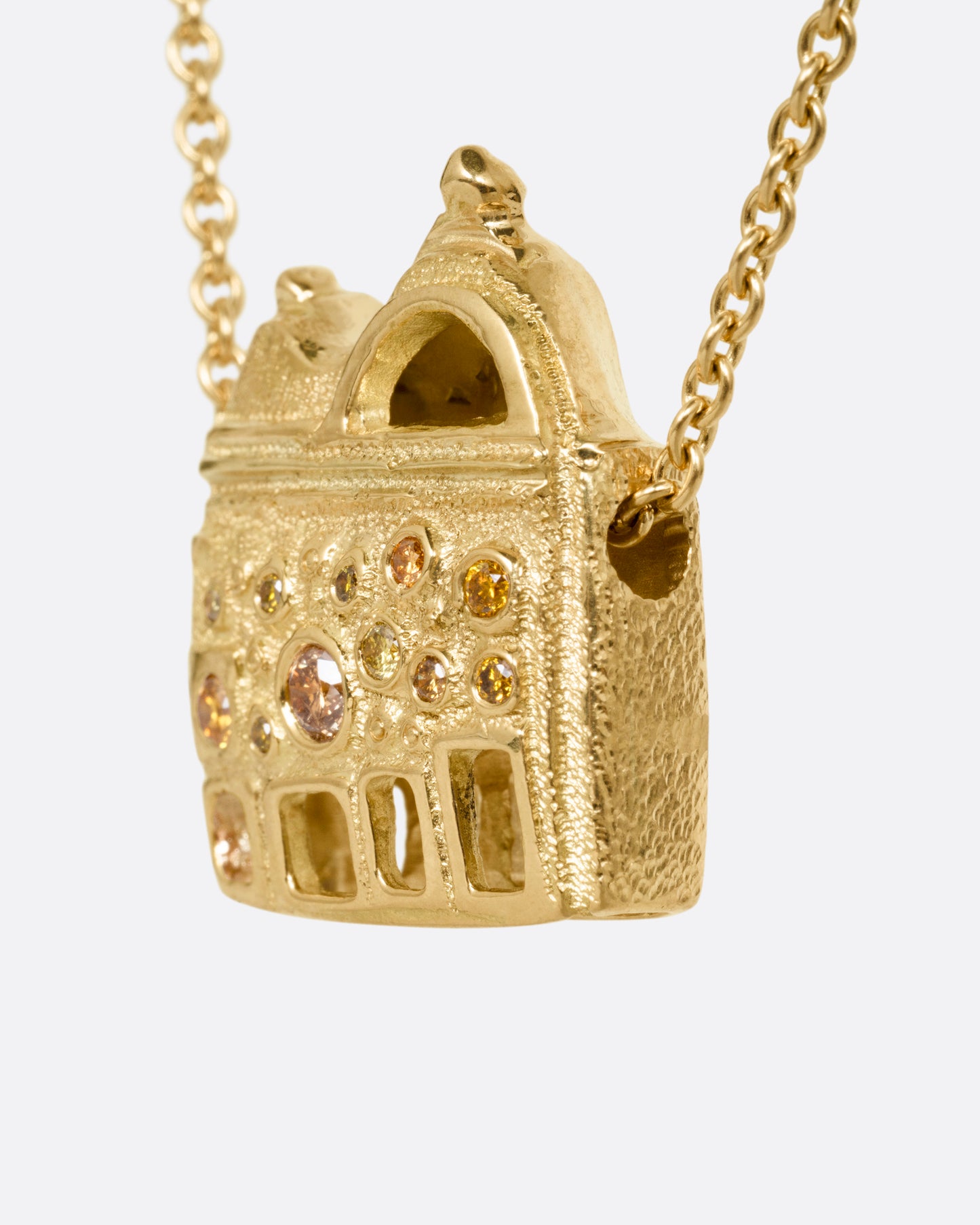A yellow gold cable chain with a house shaped pendant with open windows and multicolored diamonds, shown from the side.