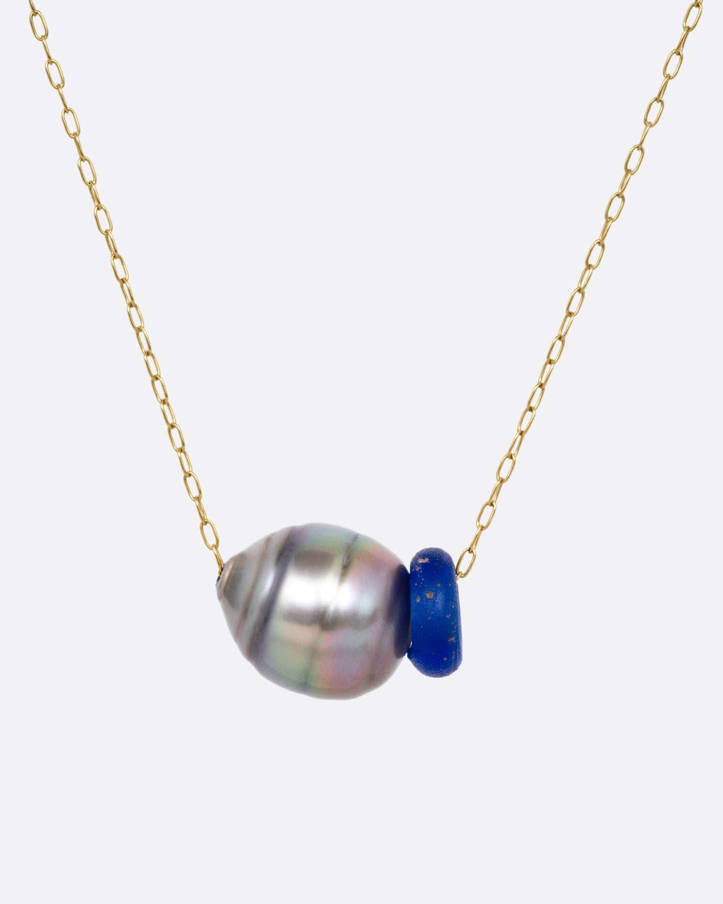 A yellow gold cable chain necklace with a blue glass antique bead and a Tahitian pearl, shown from the front.
