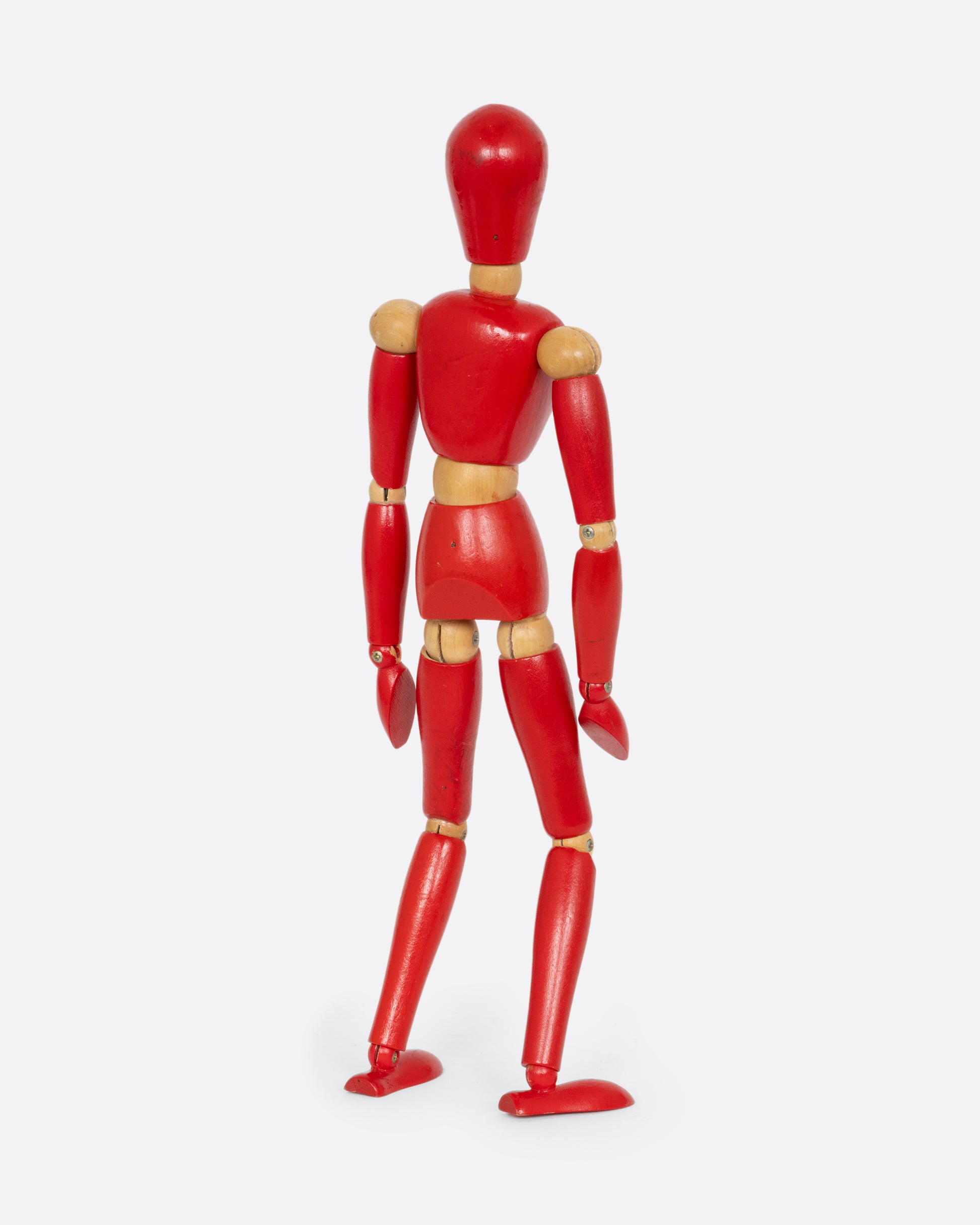 A red wooden articulated human figure. Shown standing from the back.