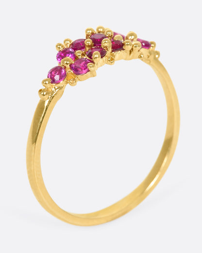 A yellow gold ring with a cluster of rubies arranged on the face. Shown from the side, standing up.