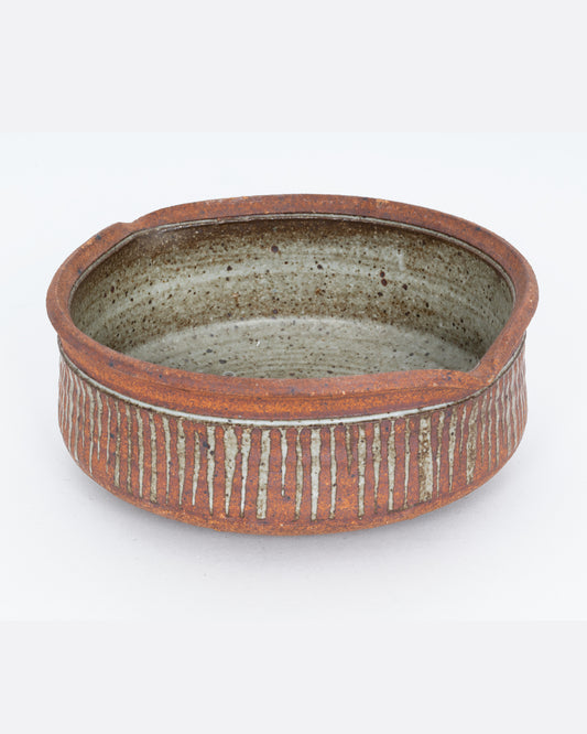 A striped ceramic serving bowl with two spouts. Shown from the side.