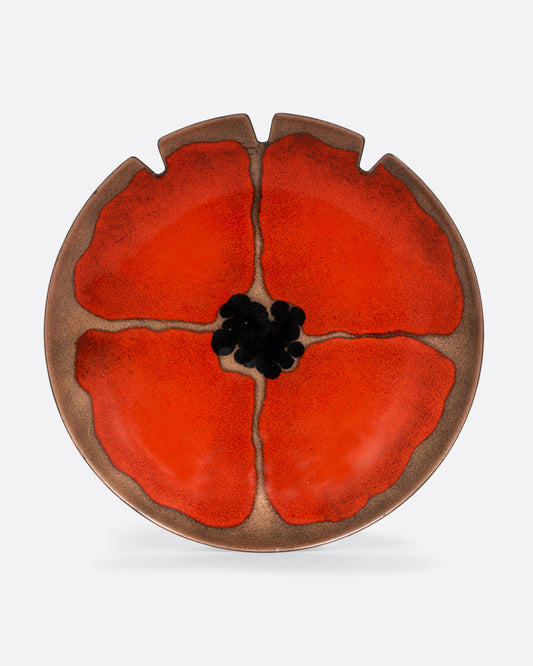 An enamel ashtray plate with a poppy flower face on it. Shown from the top on its side.