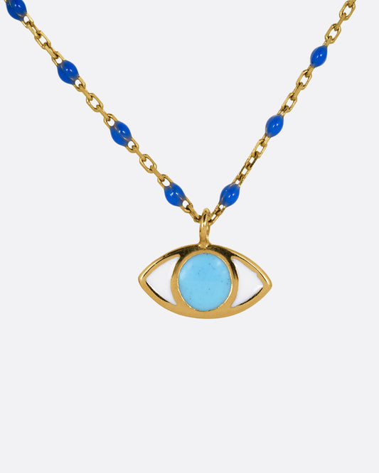 A yellow gold cable chain necklace with droplets of blue resin and an eye charm. The iris of the eye charm is turquoise blue enamel and the sclera is white. Shown from the front.
