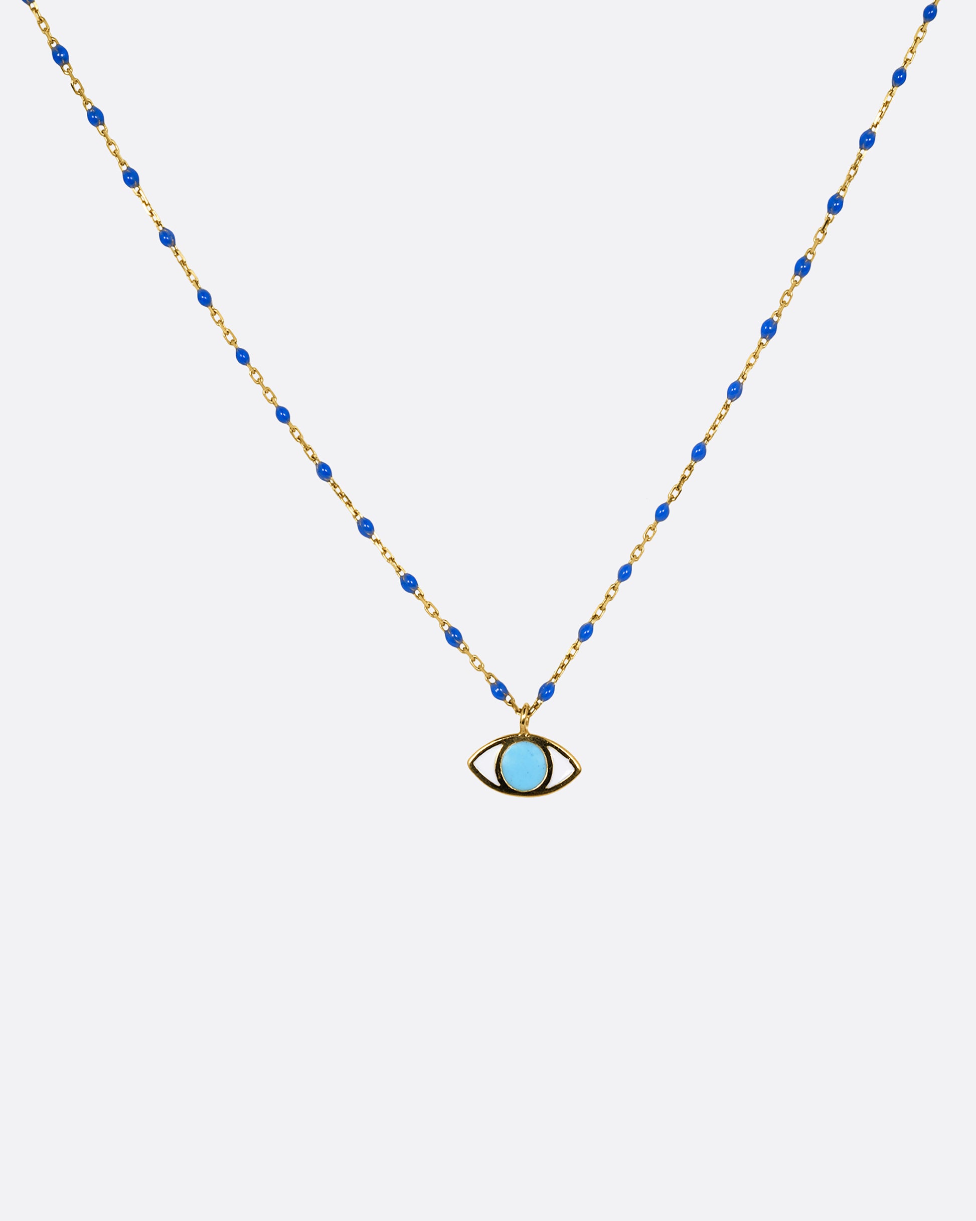 A yellow gold cable chain necklace with droplets of blue resin and an eye charm. The iris of the eye charm is turquoise blue enamel and the sclera is white. Shown from the front.