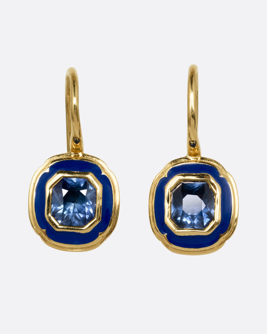 A pair of yellow gold earrings with blue sapphires at the center of a blue enamel frame. Shown from the front.