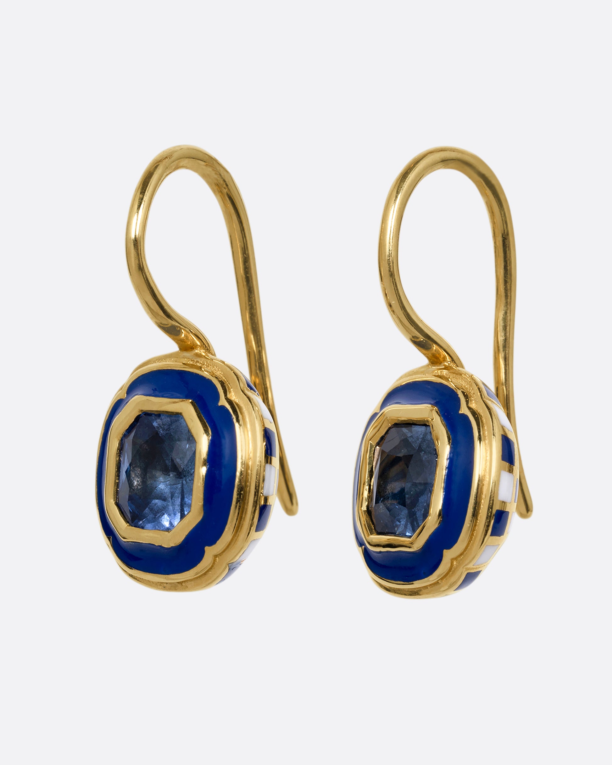 A pair of yellow gold earrings with blue sapphires at the center of a blue enamel frame. Shown from the side.