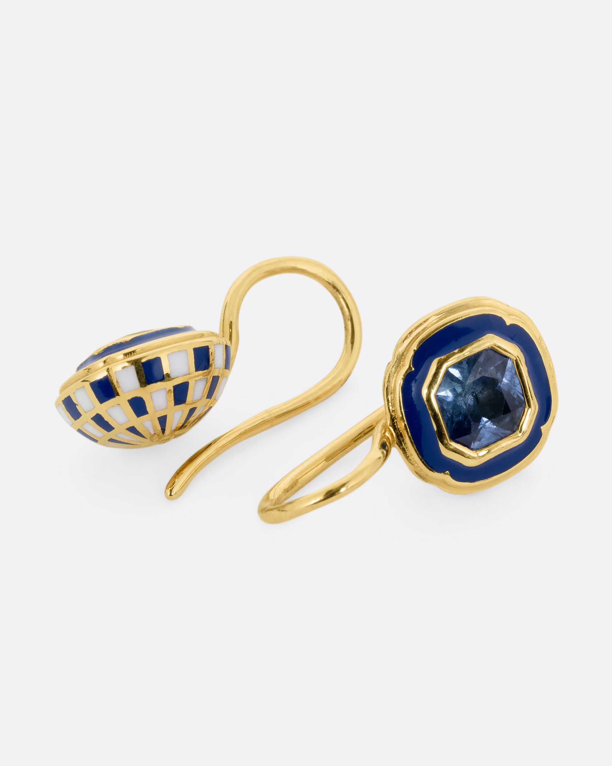 A pair of yellow gold earrings with blue sapphires at the center of a blue enamel frame. Shown laying flat.