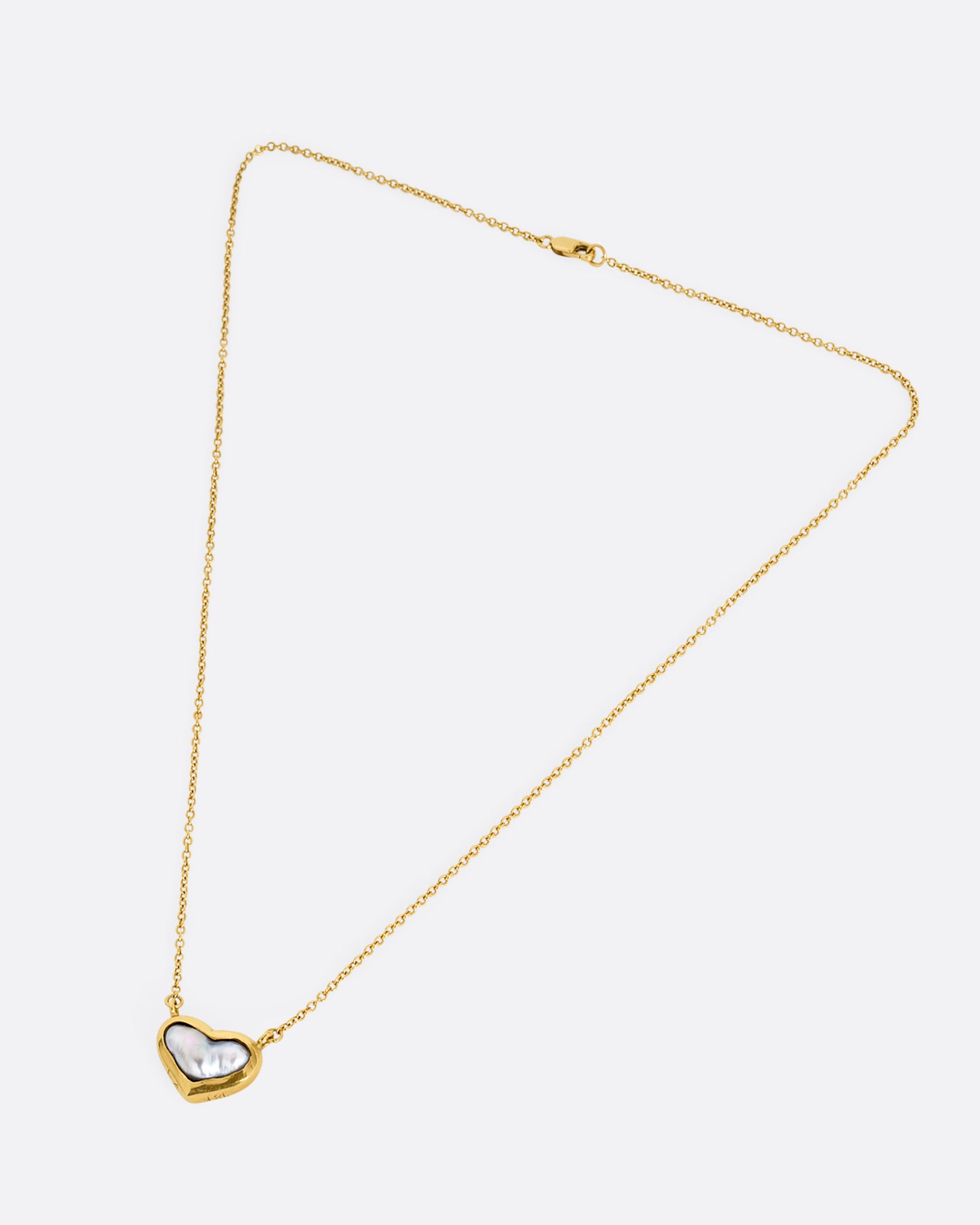 yellow gold necklace with a heart shaped pearl lying flat