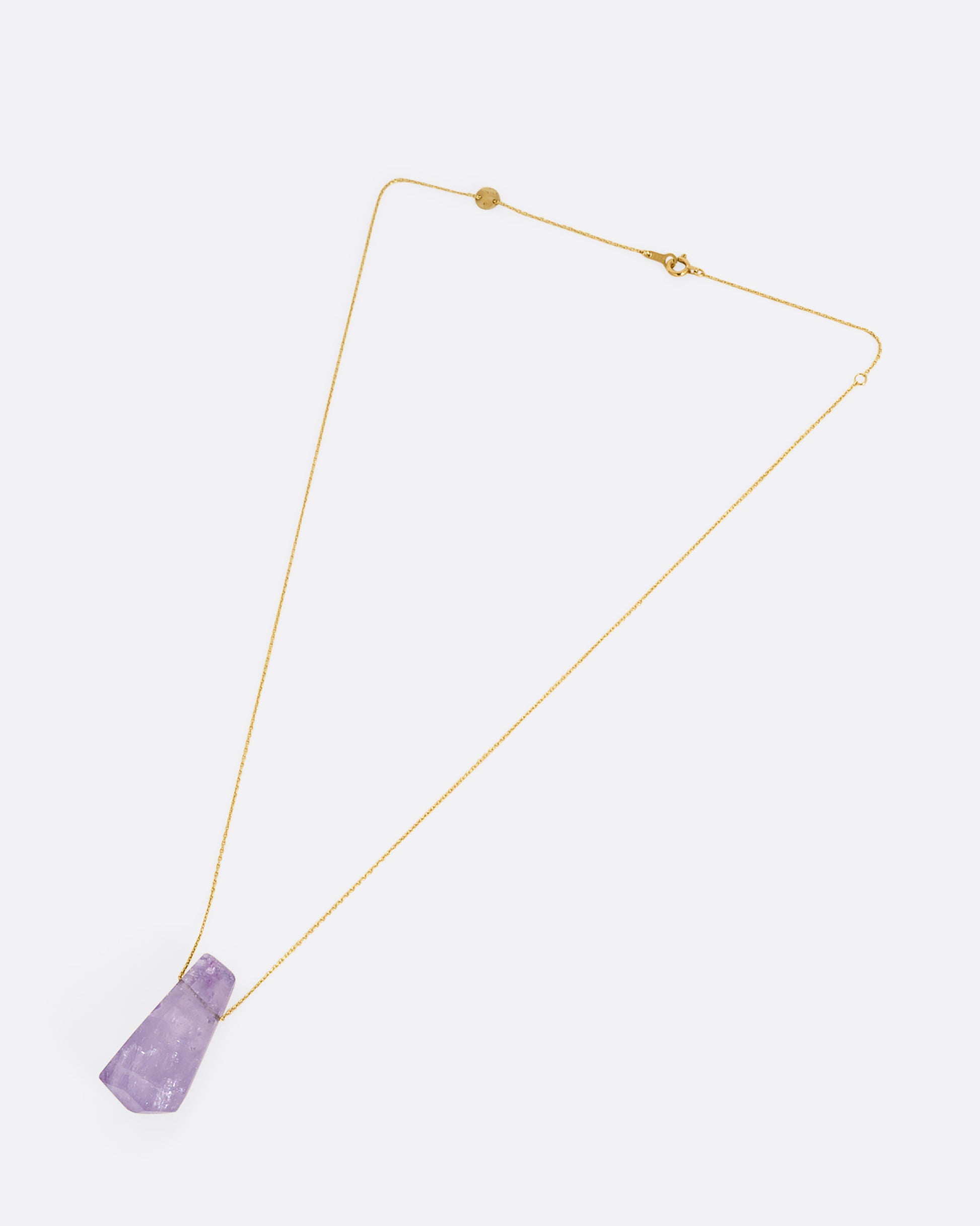 A geometric amethyst pendant hands from a dainty yellow gold chain. Shown laying flat.