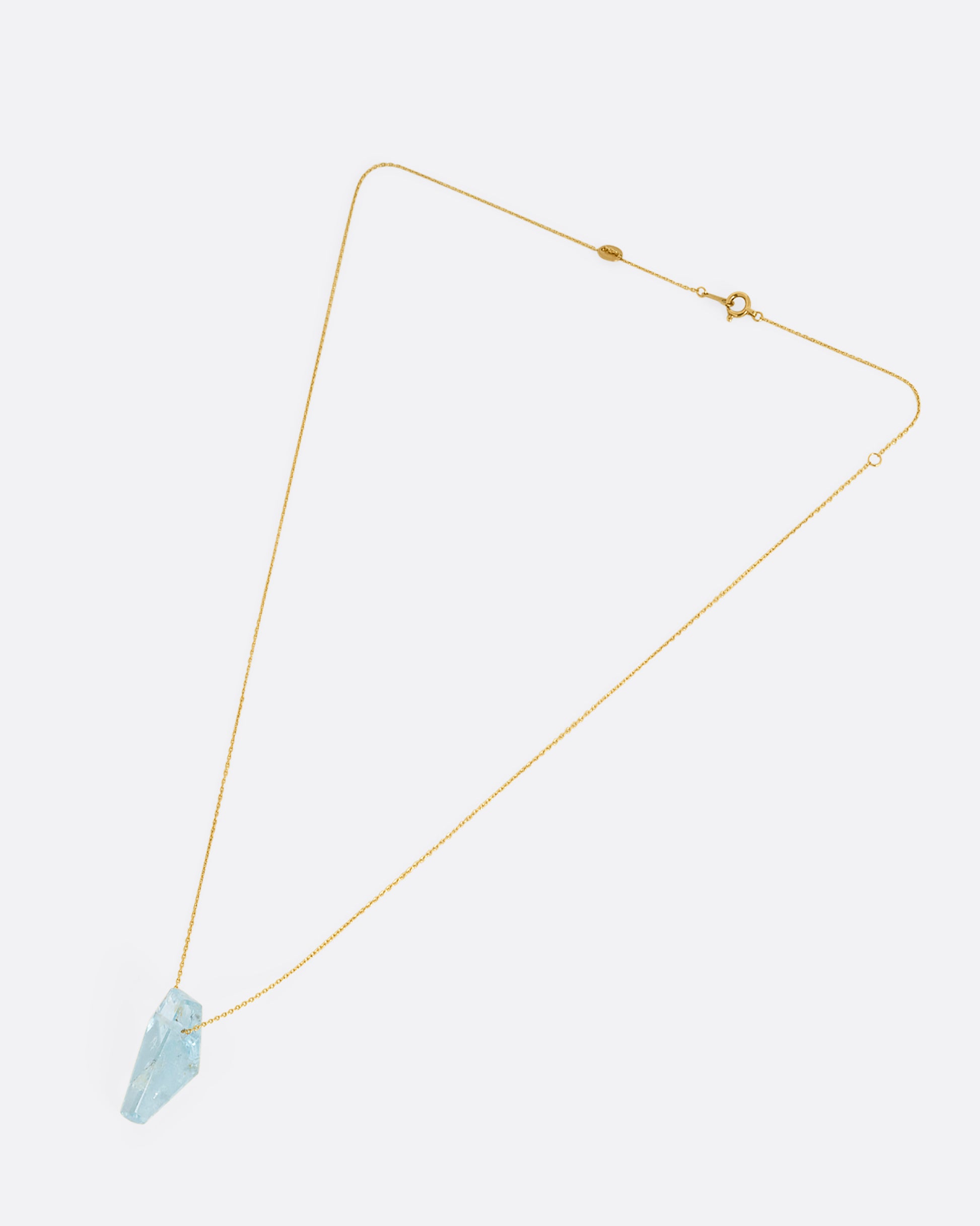 A geometric aquamarine pendant hands from a dainty yellow gold chain. Shown laying flat.