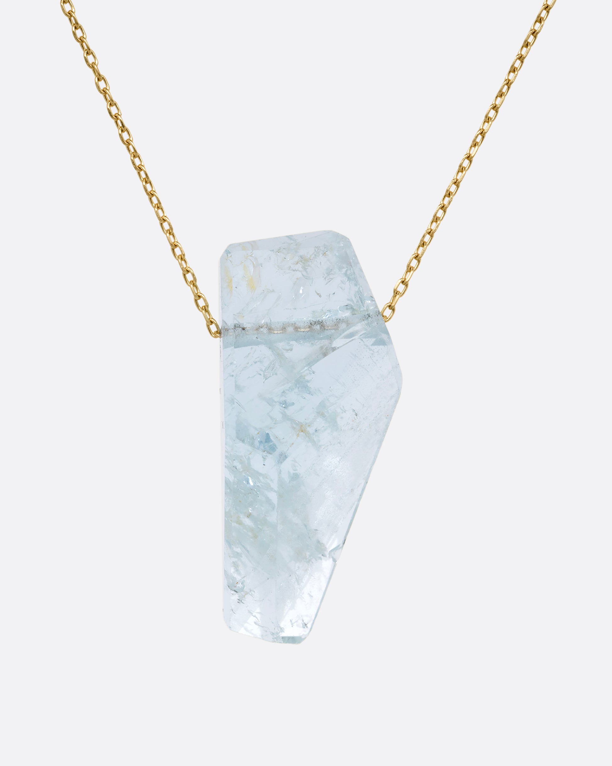 A geometric aquamarine pendant hands from a dainty yellow gold chain. Shown from the front.