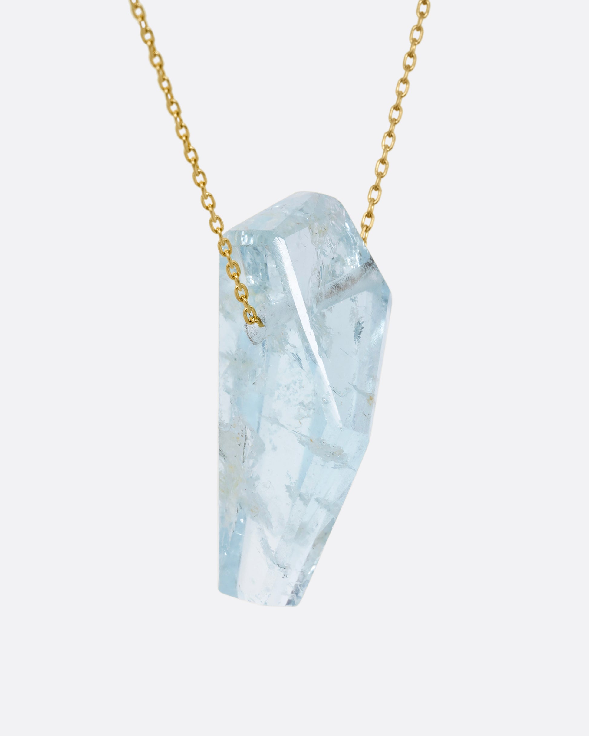 A geometric aquamarine pendant hands from a dainty yellow gold chain. Shown from the side.