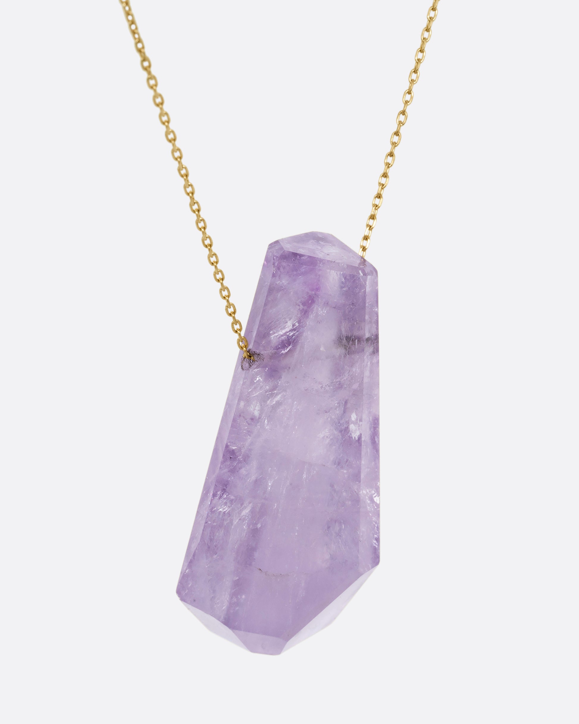 A geometric amethyst pendant hands from a dainty yellow gold chain. Shown from the side.