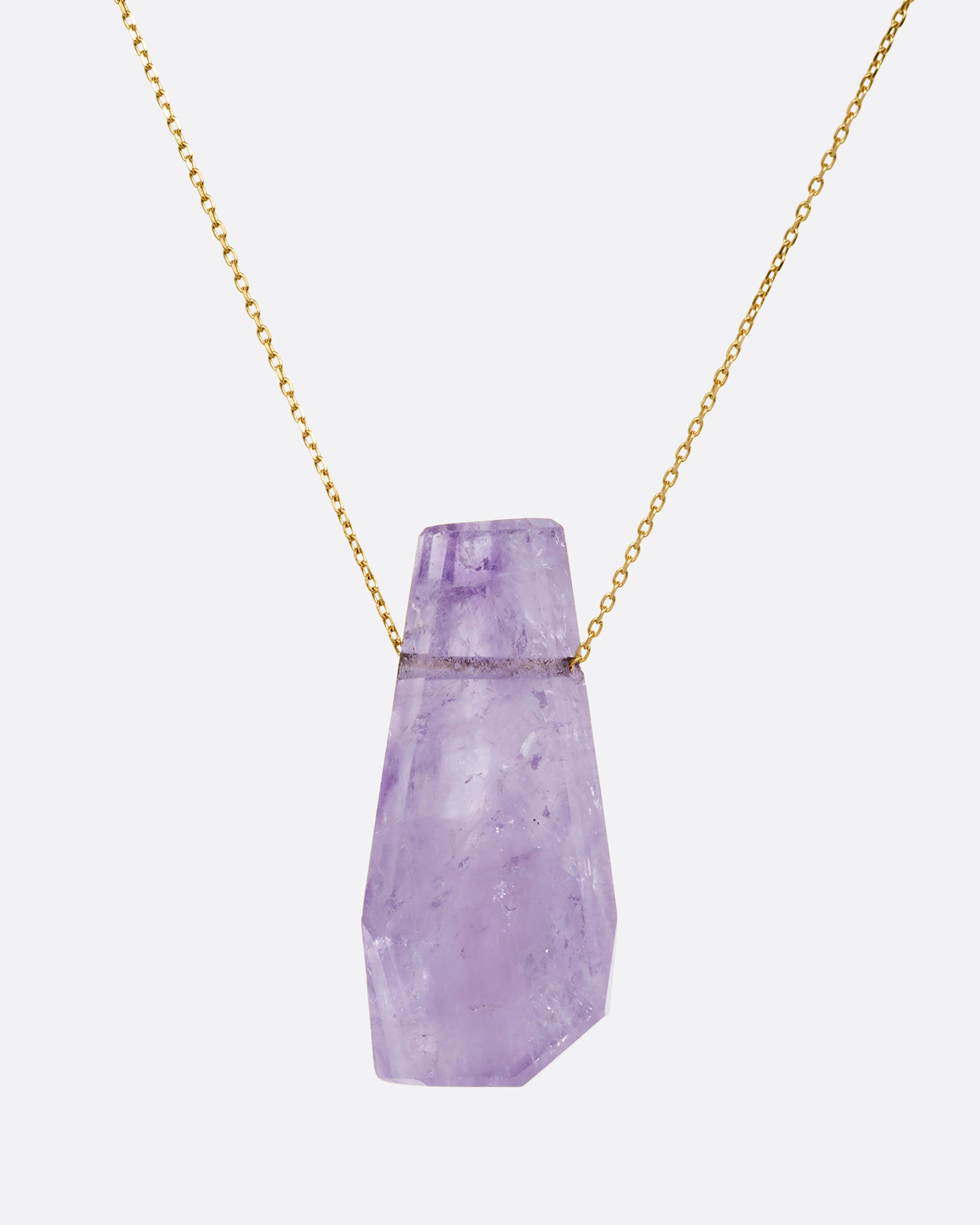 A geometric amethyst pendant hands from a dainty yellow gold chain. Shown from the front.