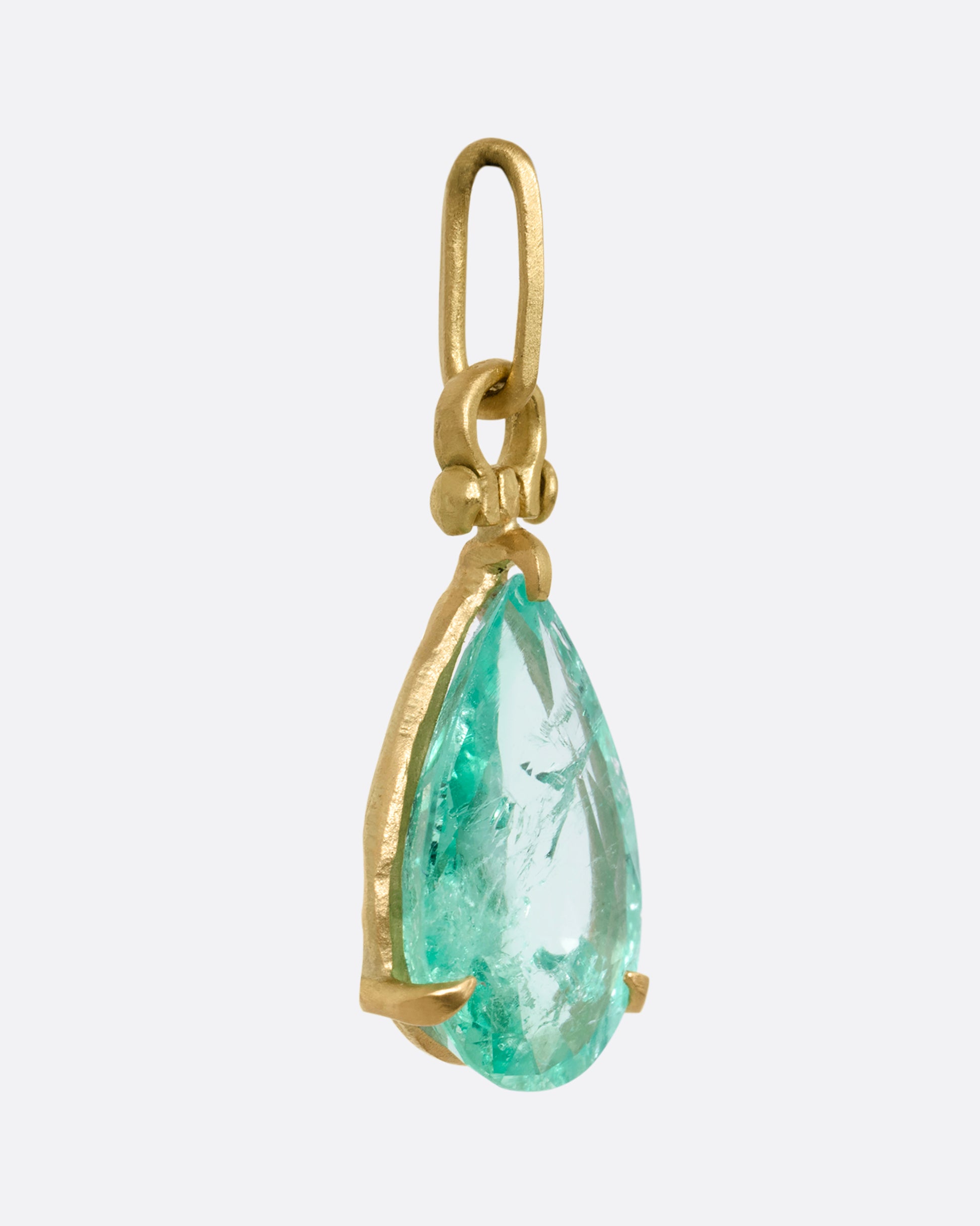 A yellow gold tear drop shaped prong set emerald pendant. Shown from the side.