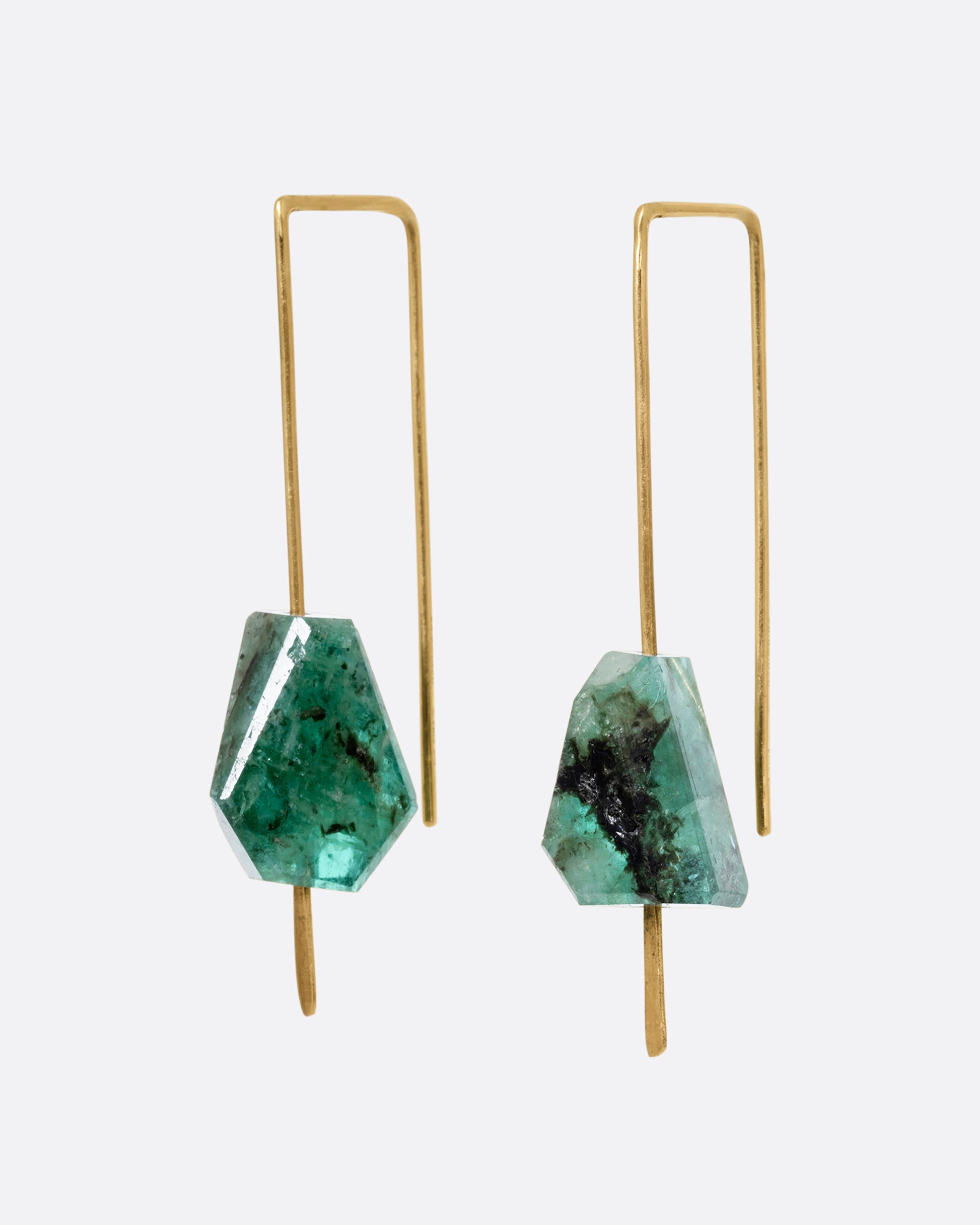 A pair of yellow gold wire earrings with a geometric emerald on each. Shown from the side.