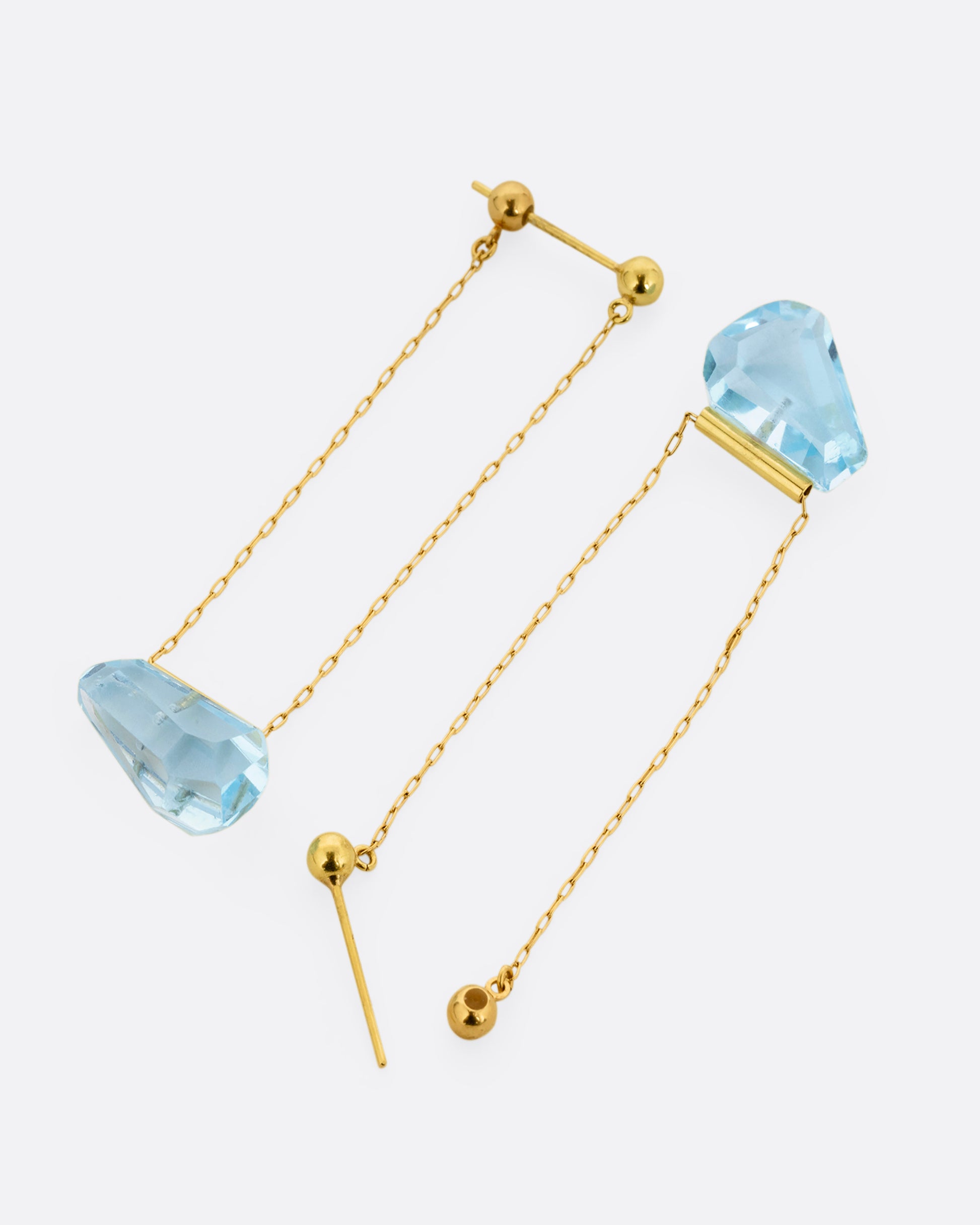 A pair of yellow gold chain earrings with free form blue topaz. Shown laying flat.