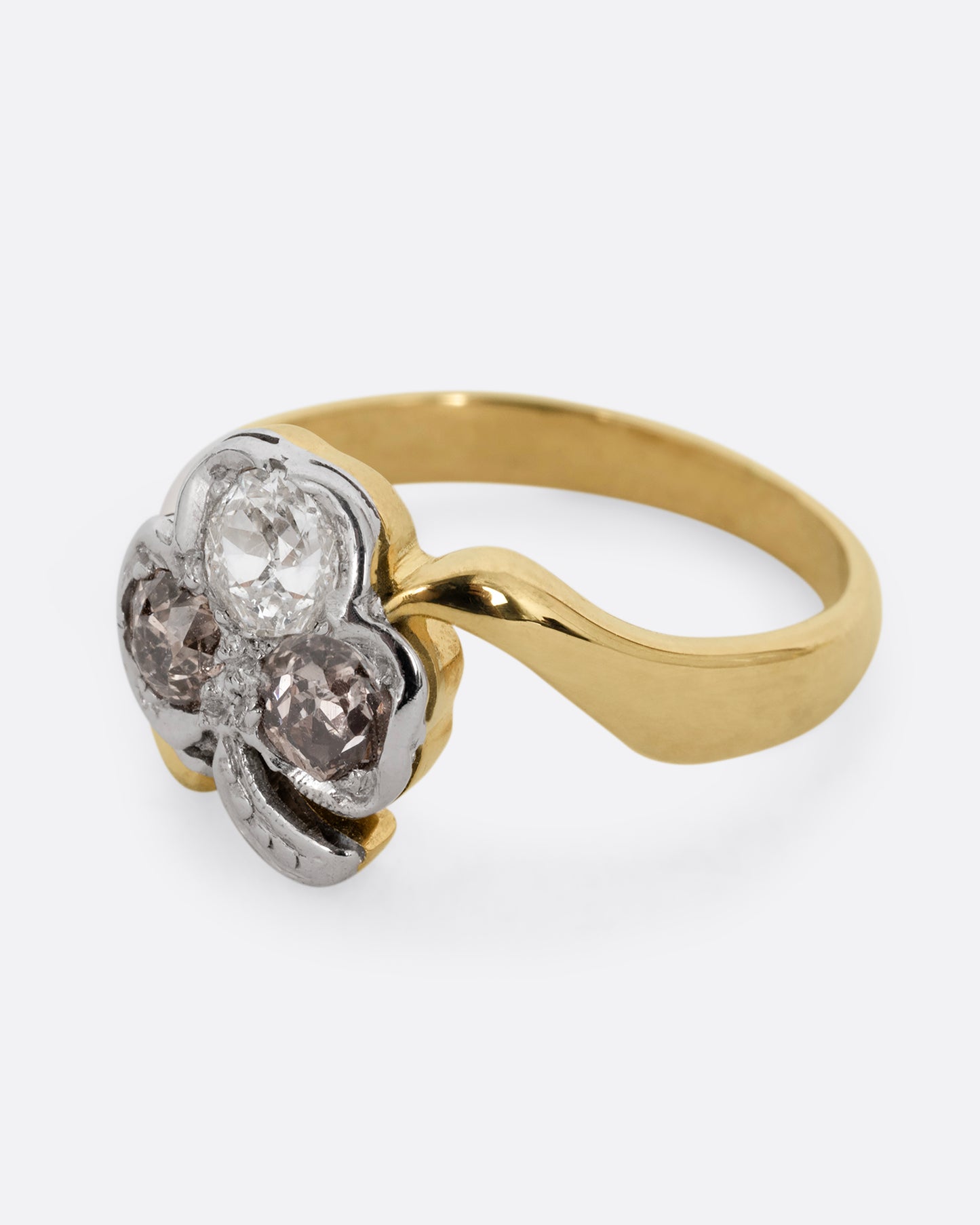 A yellow gold ring with a white gold three leaf clover at the center, made of white and cognac diamonds. Shown from the side.