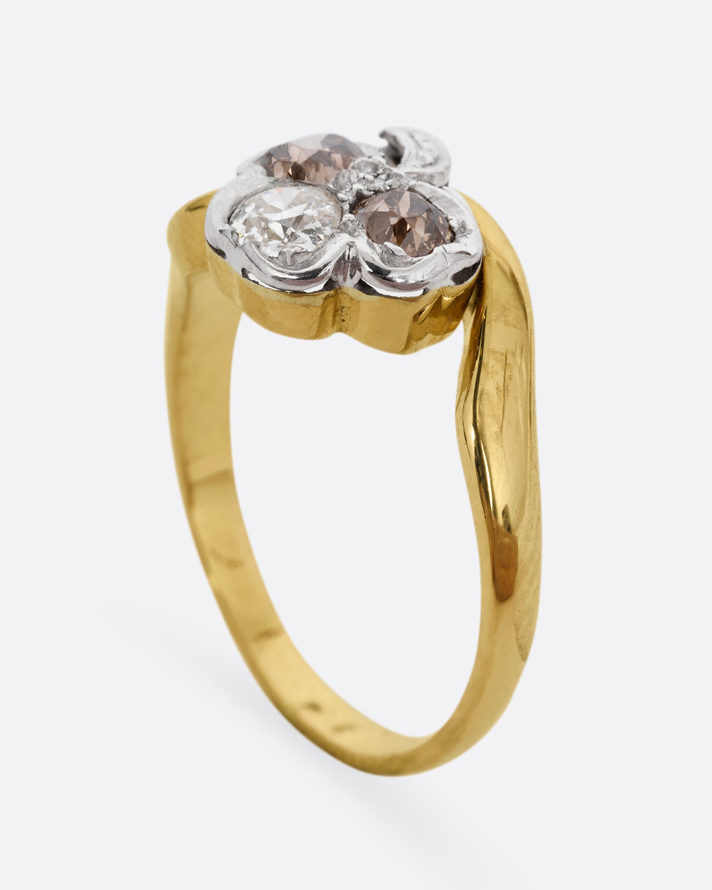 A yellow gold ring with a white gold three leaf clover at the center, made of white and cognac diamonds. Shown from the side, standing up.