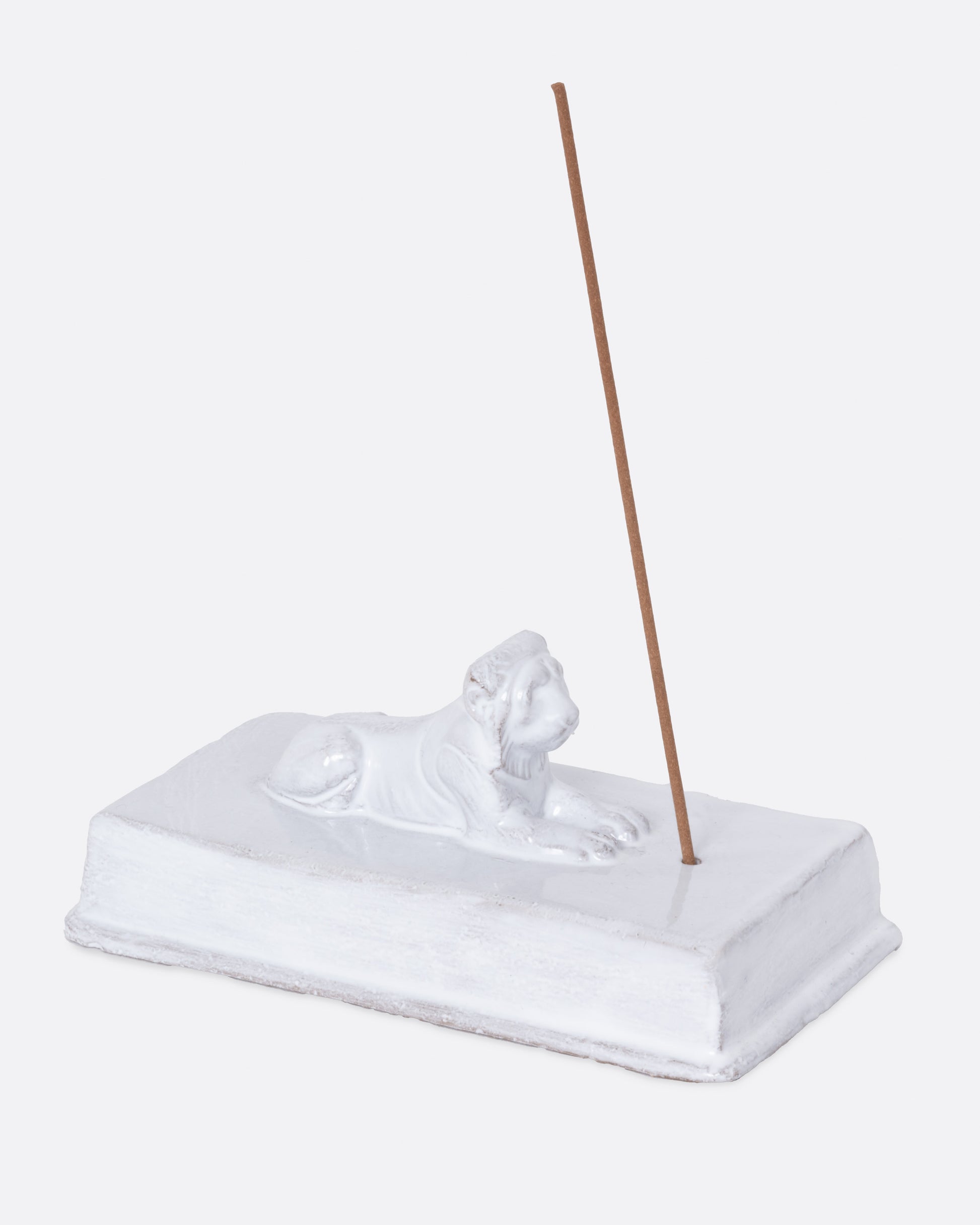 A white rectangular incense holder with a lion on top. Shown from the side with an incense stick in it.
