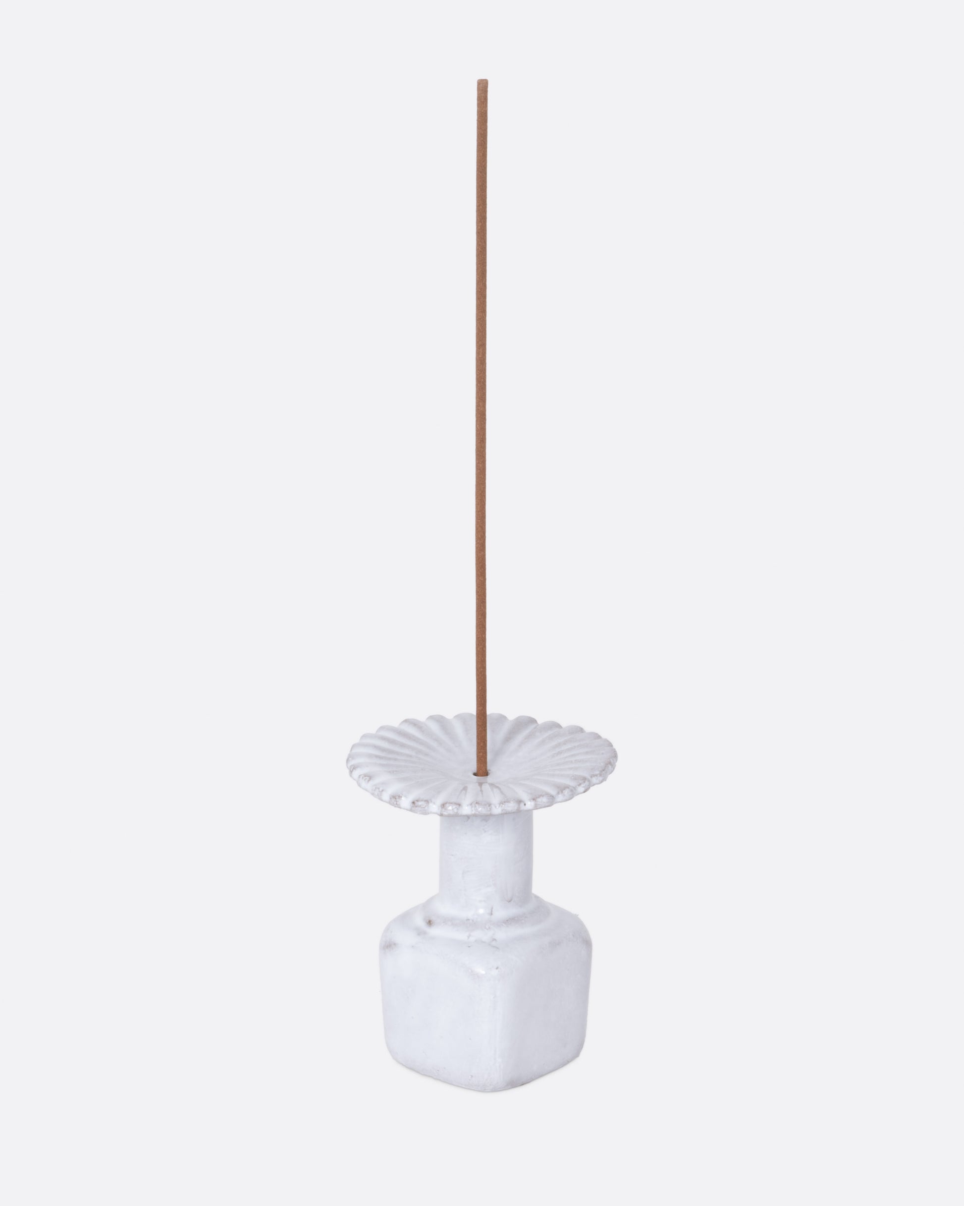  A white ceramic fluted incense holder, shown from the side with an incense stick in it.