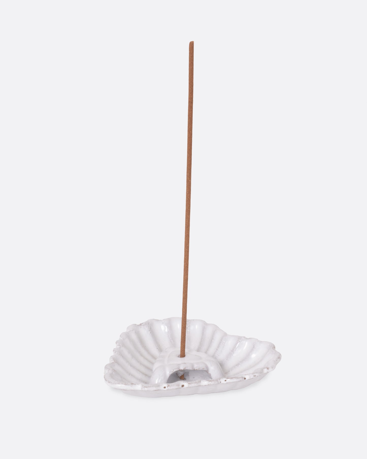 A white heart shaped incense holder, shown from the side with an incense stick in it. 