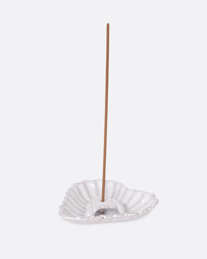 A white heart shaped incense holder, shown from the side with an incense stick in it. 