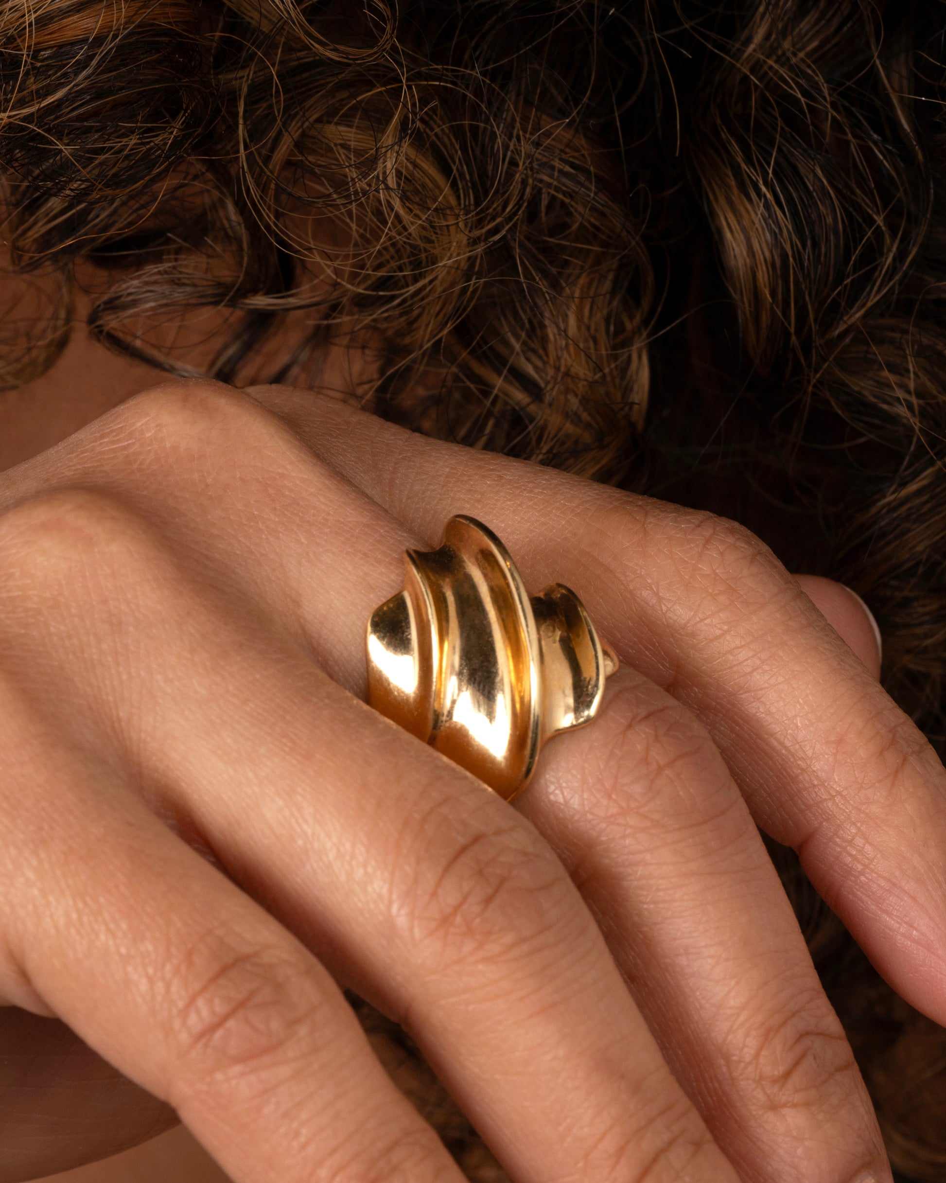 A chunky yellow gold wave ring. Shown worn on a hand.