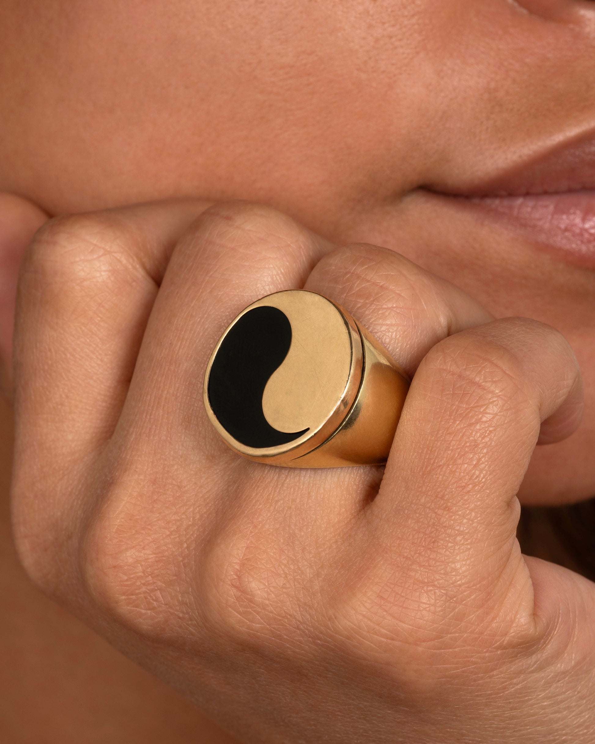 A yellow gold ring with a yin yang symbol made of onyx. Shown on a hand.