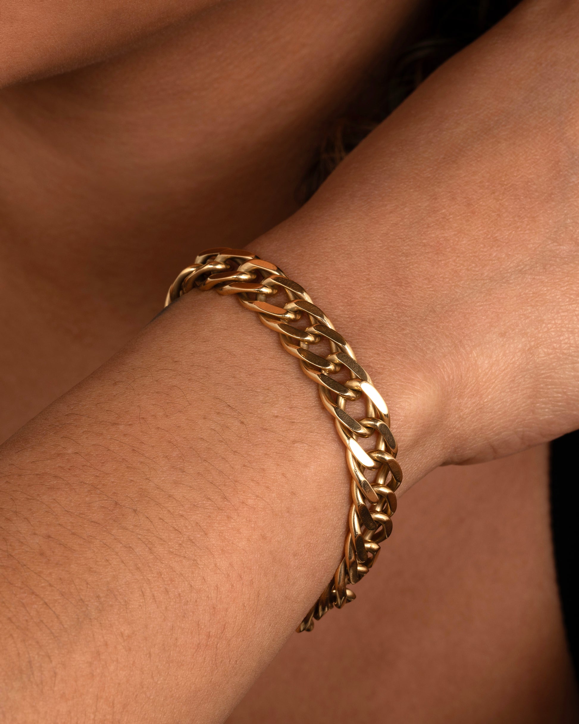 A yellow gold double curb chain bracelet. Shown worn around a wrist.