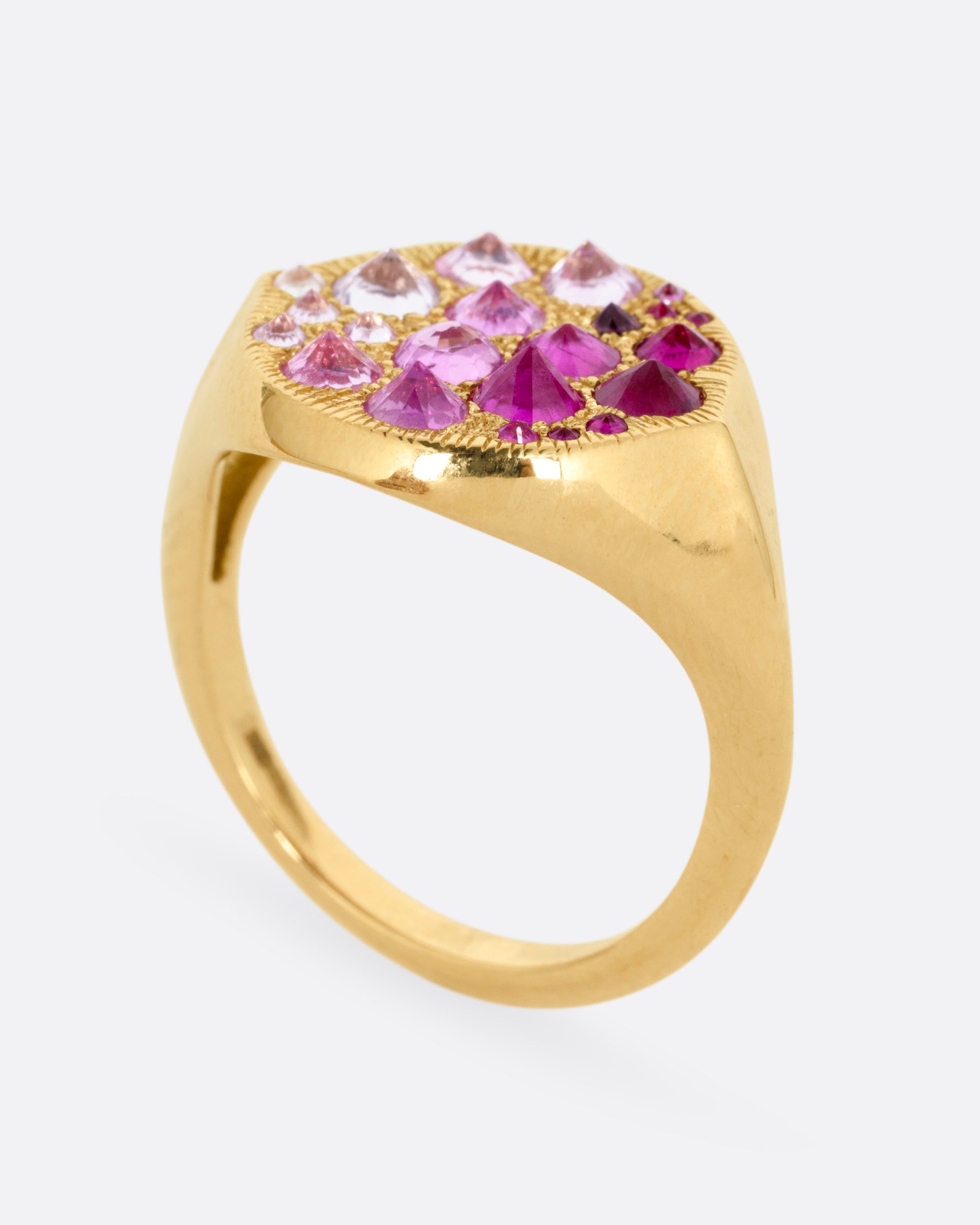 A yellow gold signet eye-shaped ring with an ombré of reverse set sapphires and rubies. Shown from the side standing up.