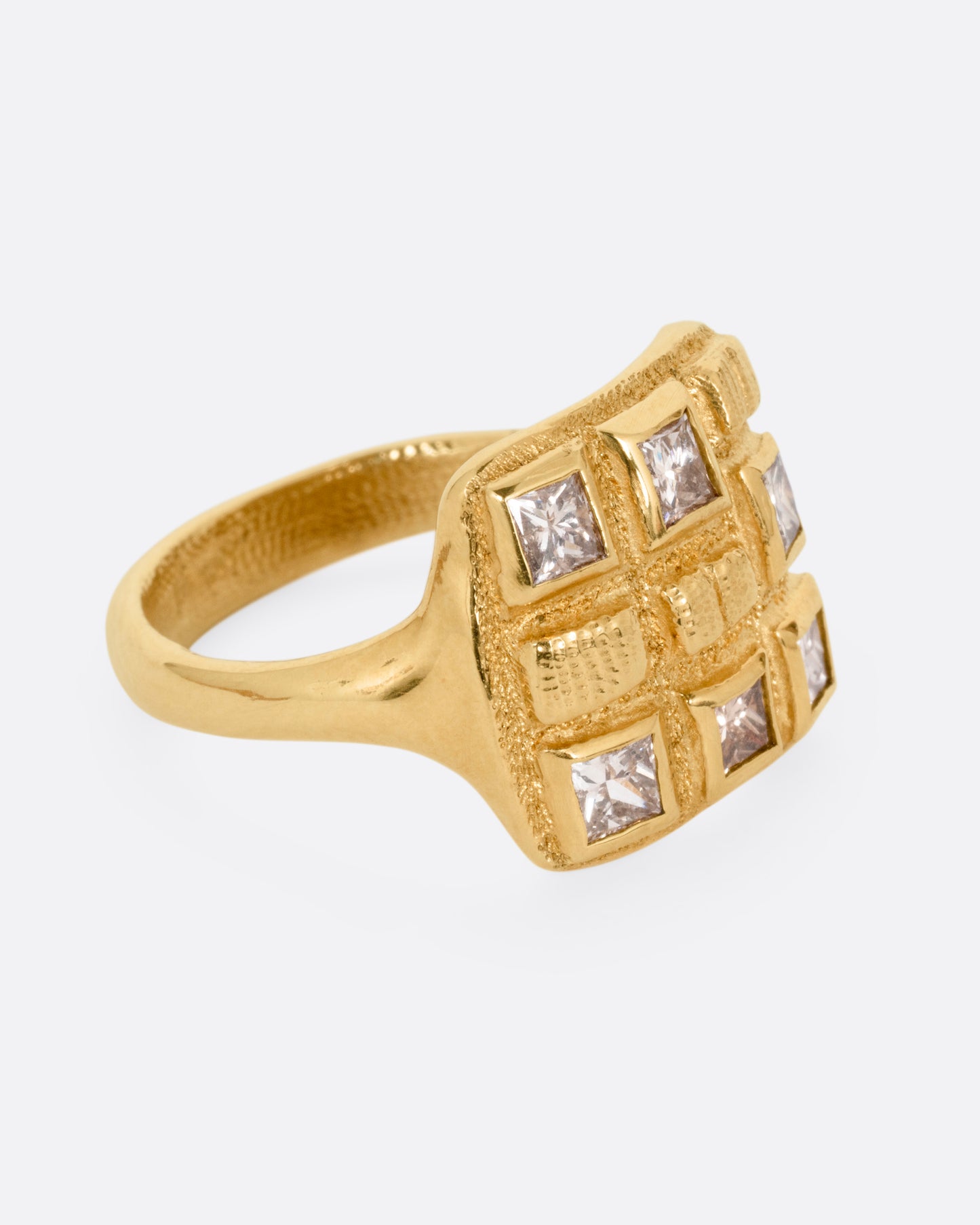 A yellow gold ring with princess cut brown diamonds and raised textural squares across its broad face. Shown from the side.