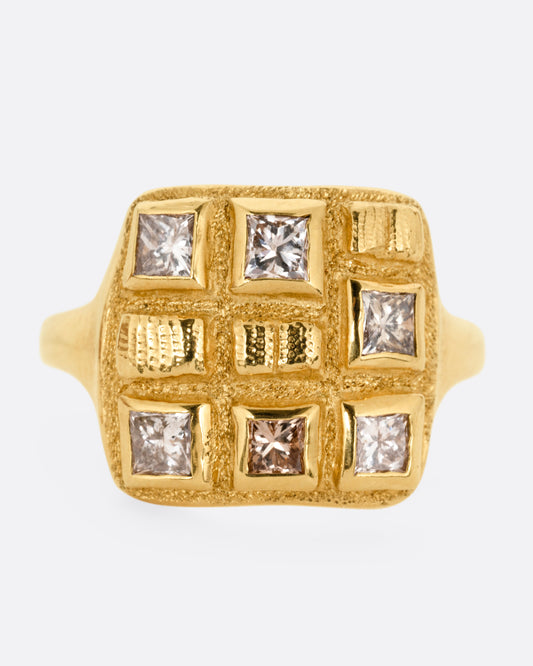 A yellow gold ring with princess cut brown diamonds and raised textural squares across its broad face. Shown from the front.