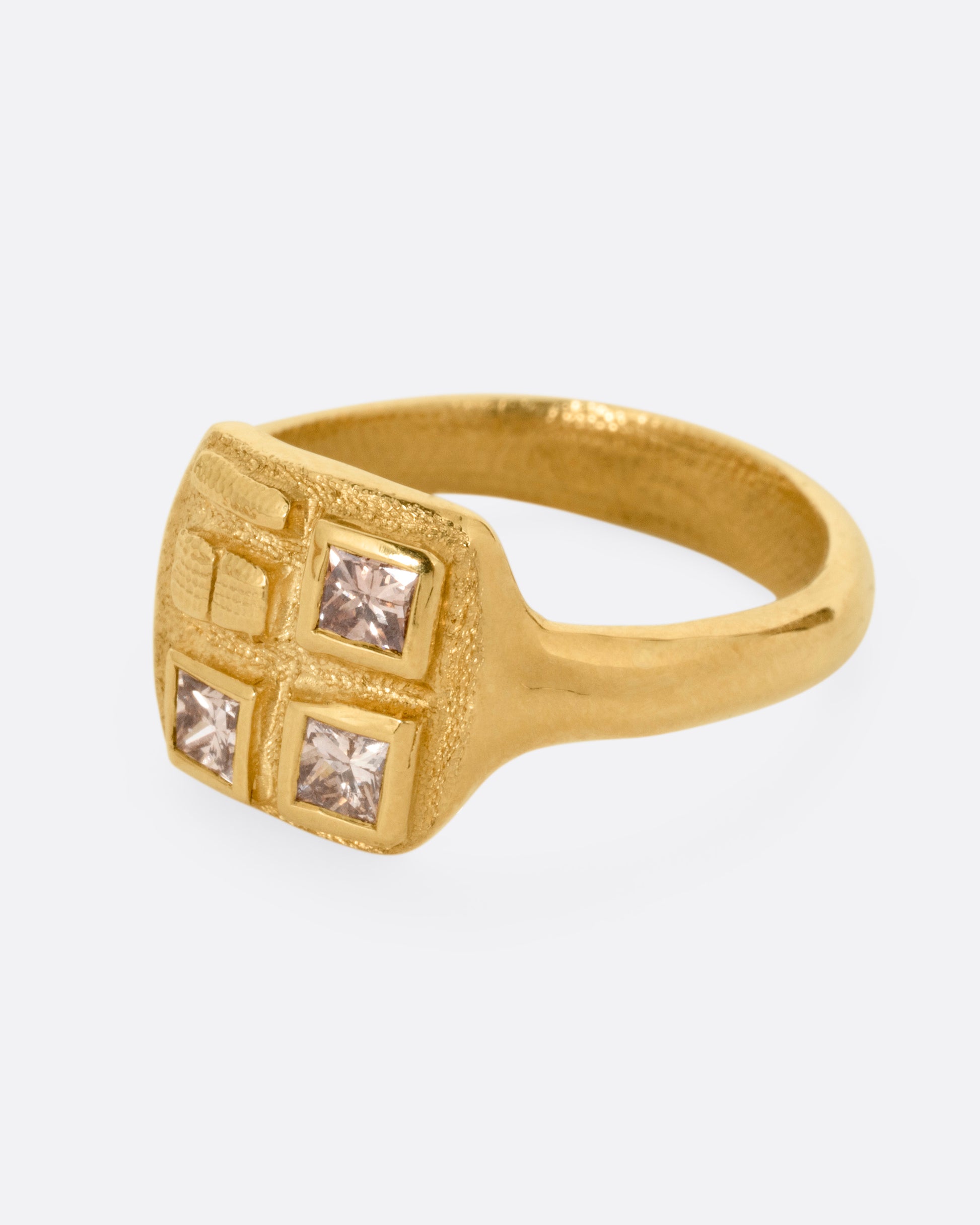 A yellow gold ring with three square diamonds on its square face, shown from the side.