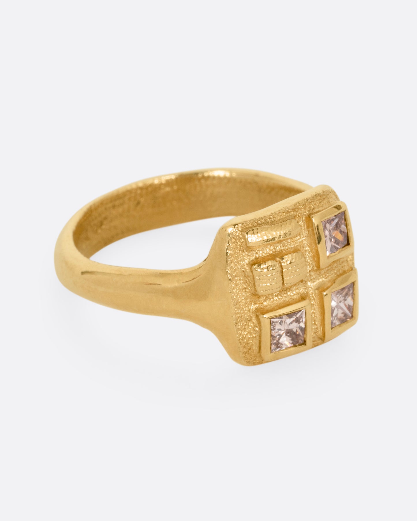 A yellow gold ring with three square diamonds on its square face, shown from the side.