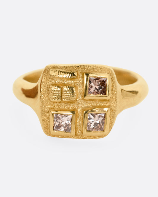 A yellow gold ring with three square diamonds on its square face, shown from the front.