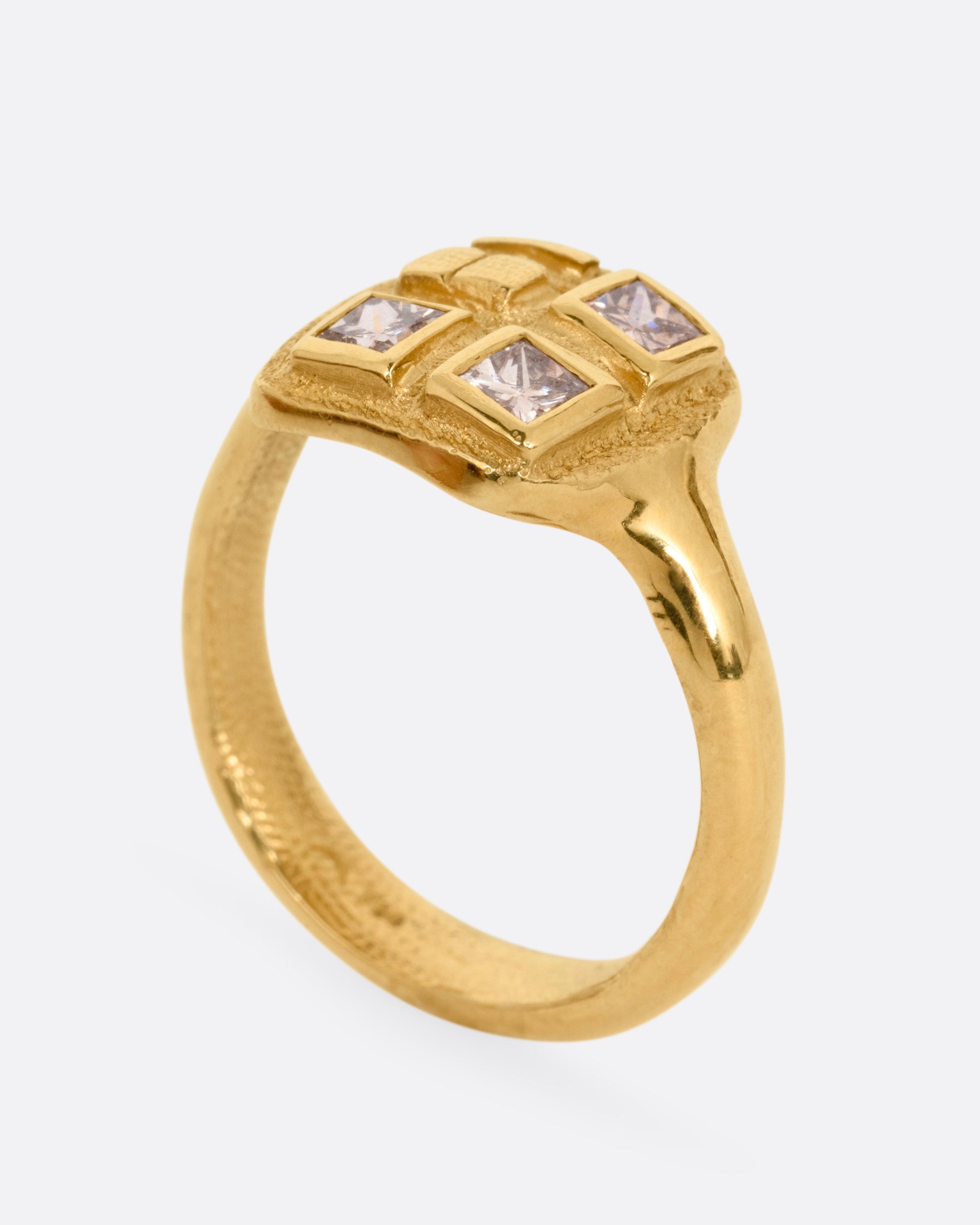 A yellow gold ring with three square diamonds on its square face, shown from the side standing up.